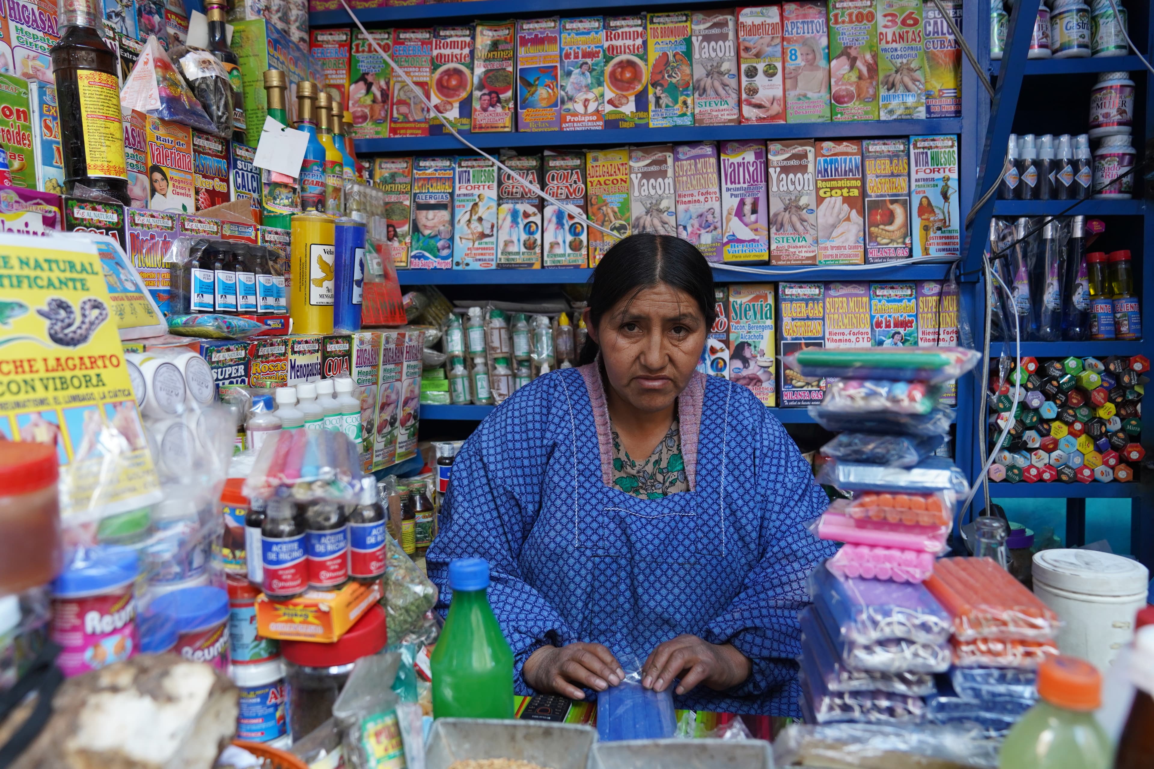 Morales supporter wearing a blue top stands in a fully-stocked shop with bright and colorful products stacked behind her.