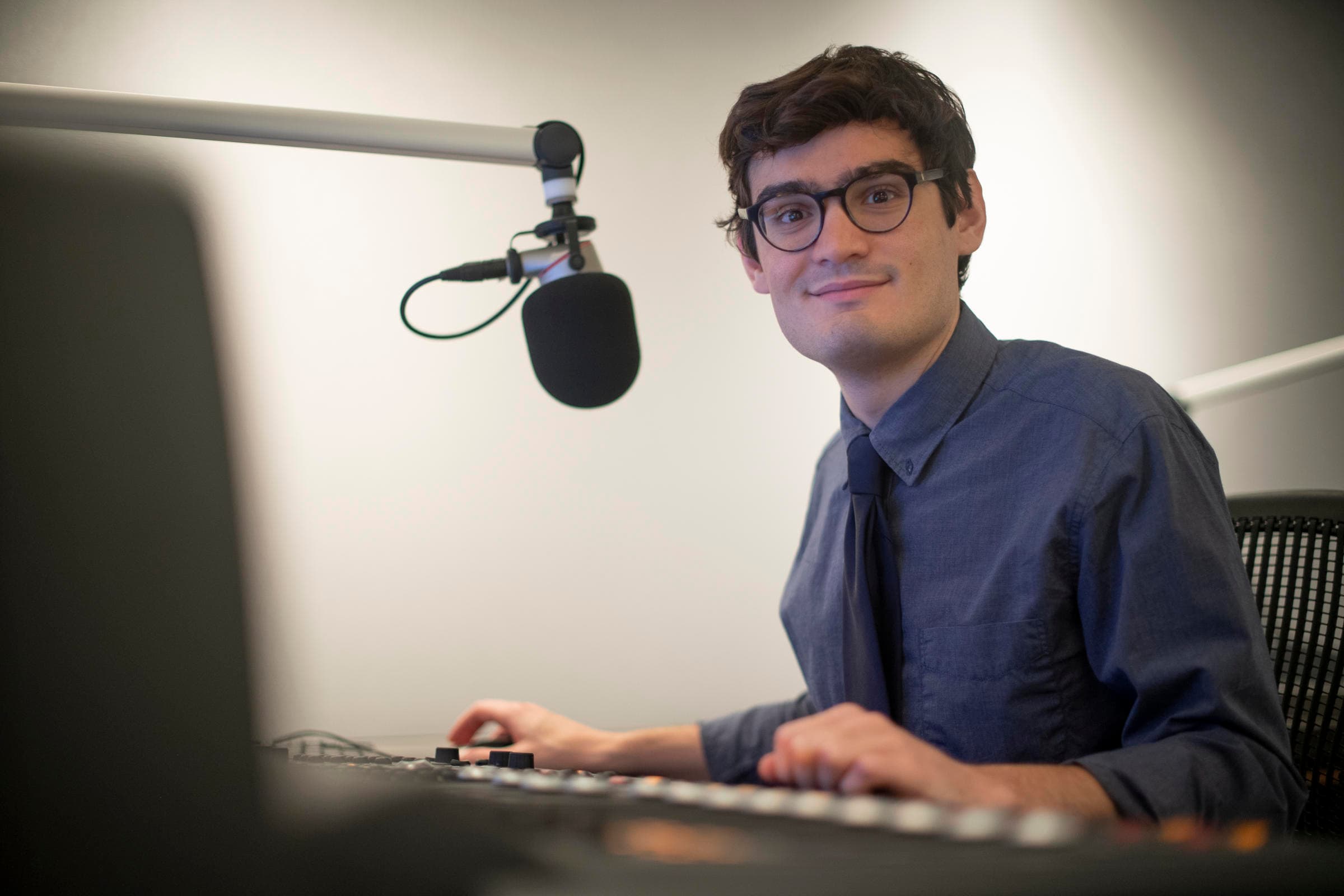A man wearing glasses poses at a microphone for a photo
