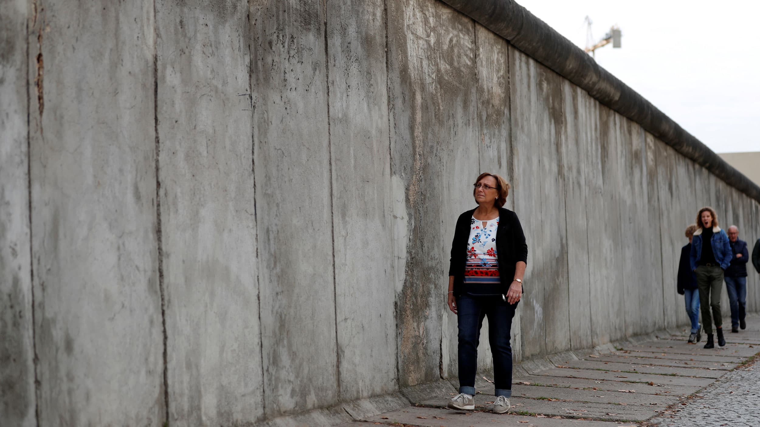 A woman walks along a tall concrete wall