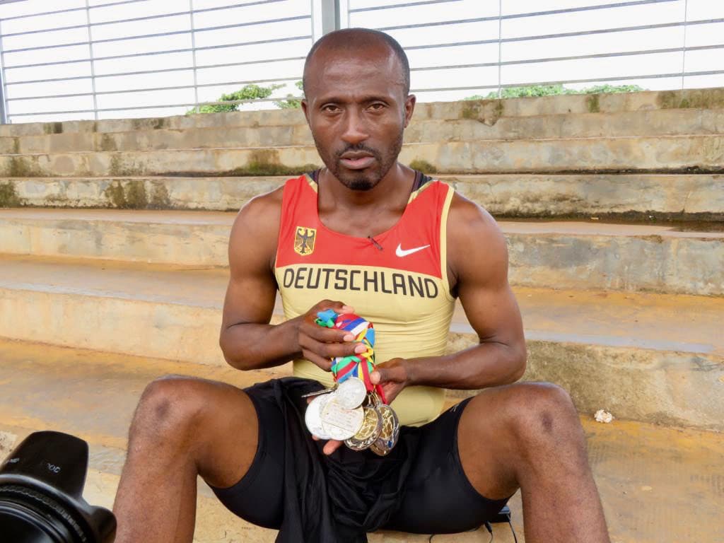 A man wearing a Deutschland jersey and holds many medals in his hands.