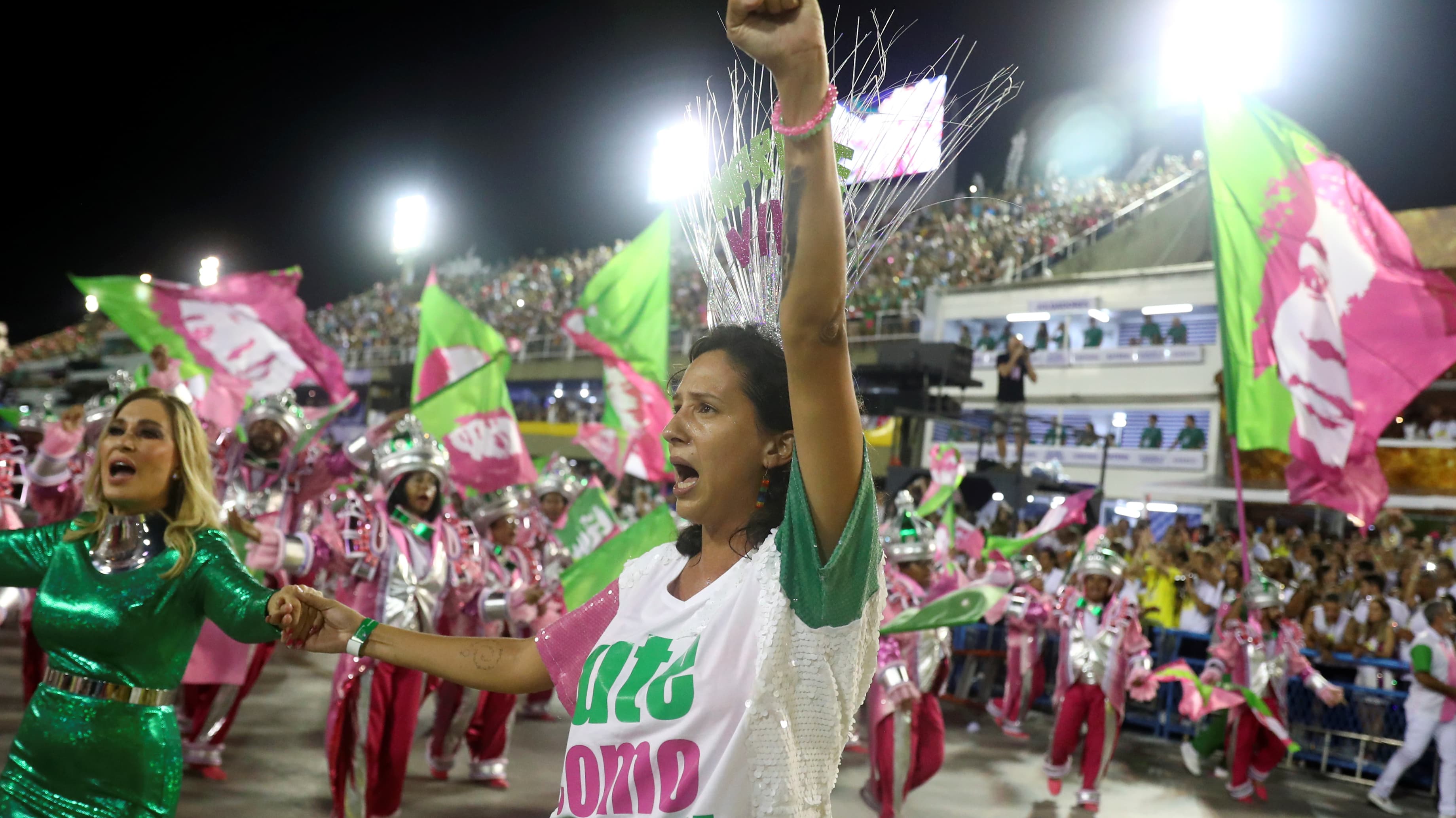 A woman raises her fist and shouts near a woman wearing dazzling green dress.