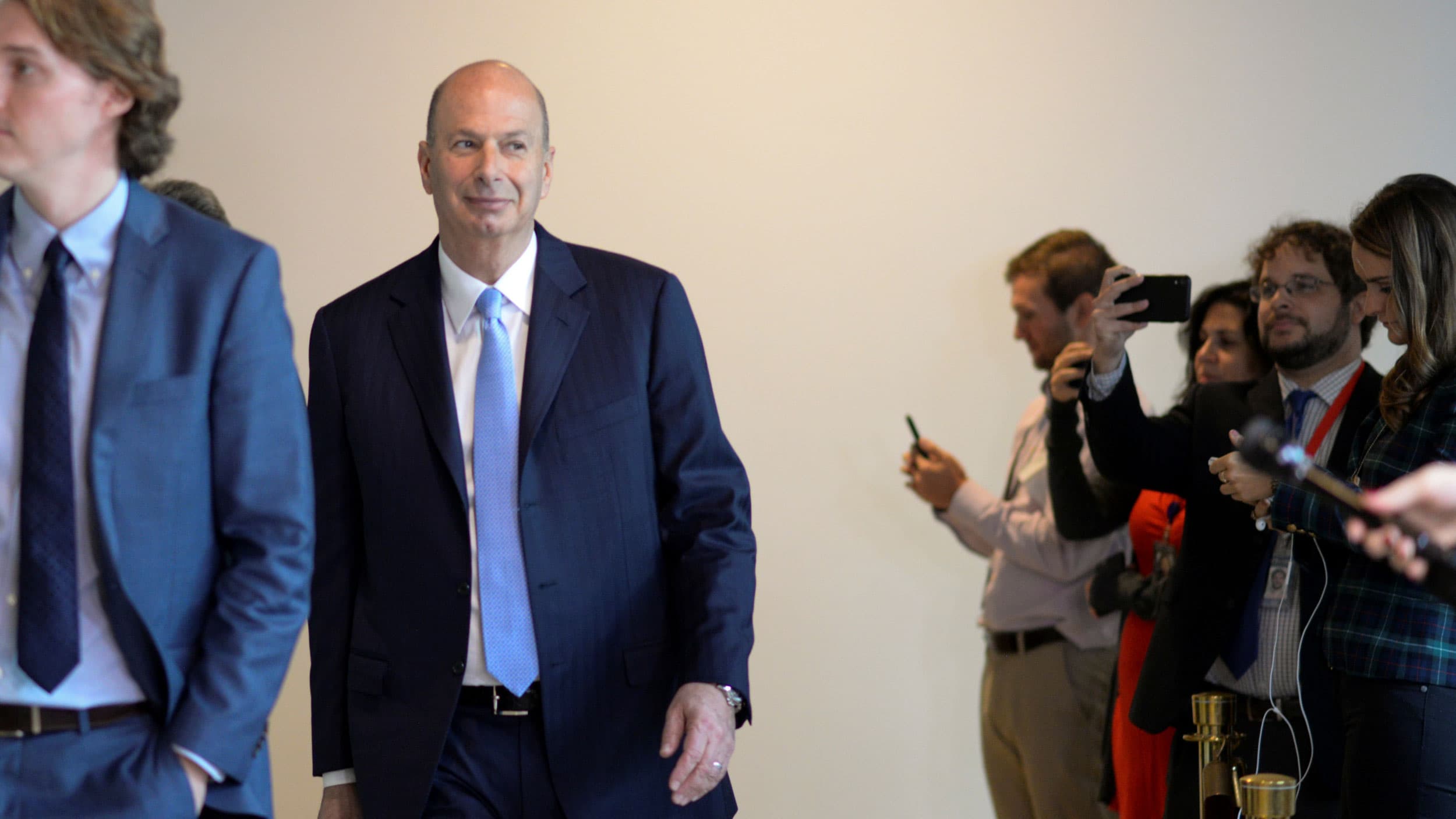 a man in a suit walks with people standing by