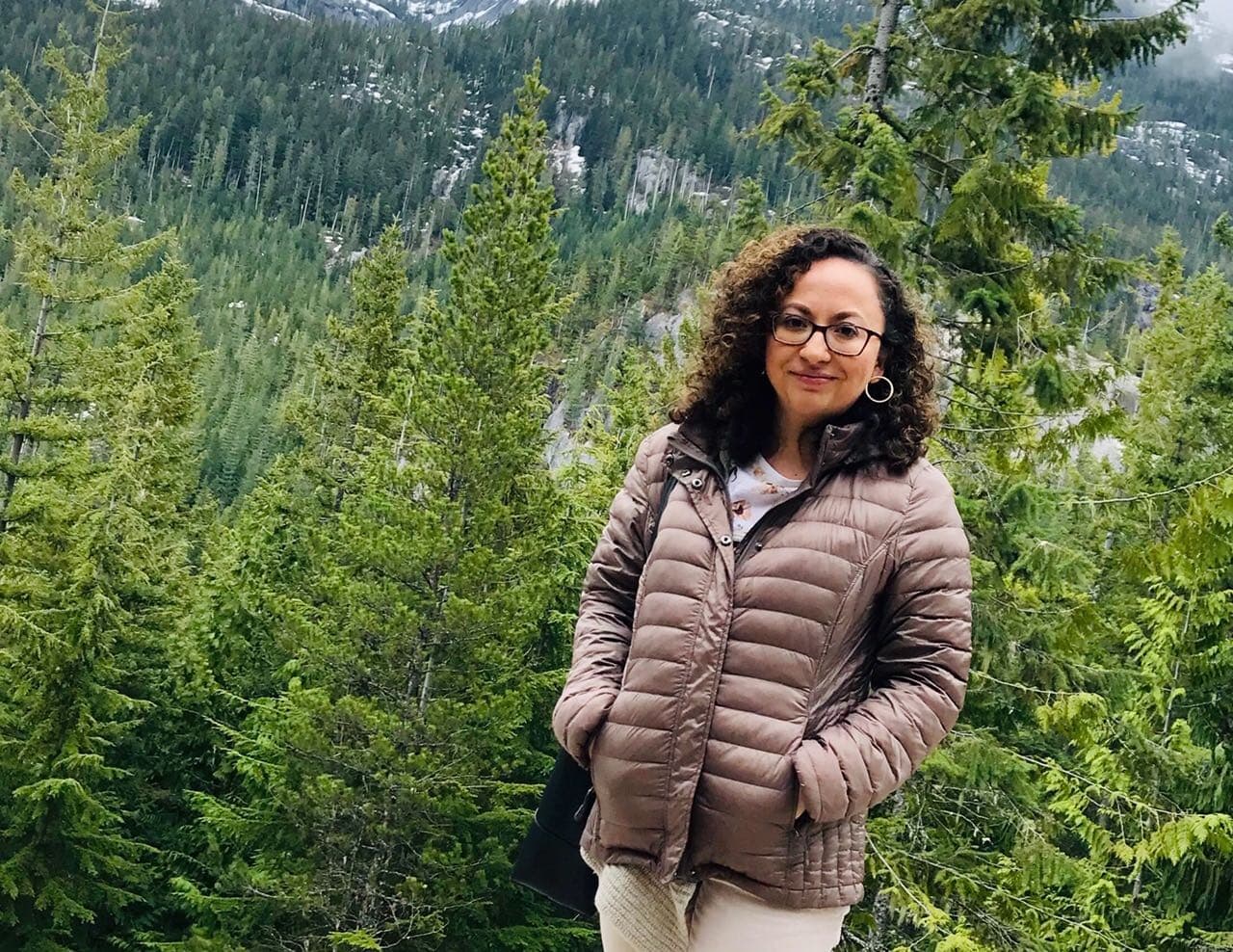A woman stands on a mountain overlook.