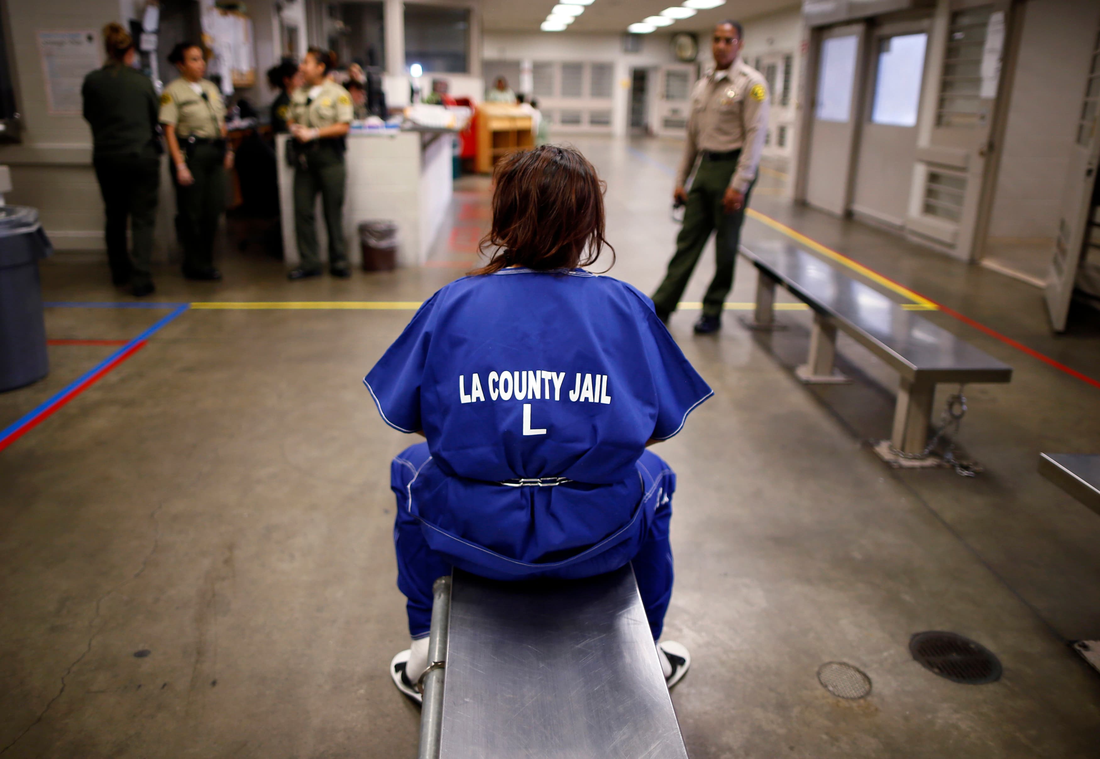 A woman sits on a bench in jail.