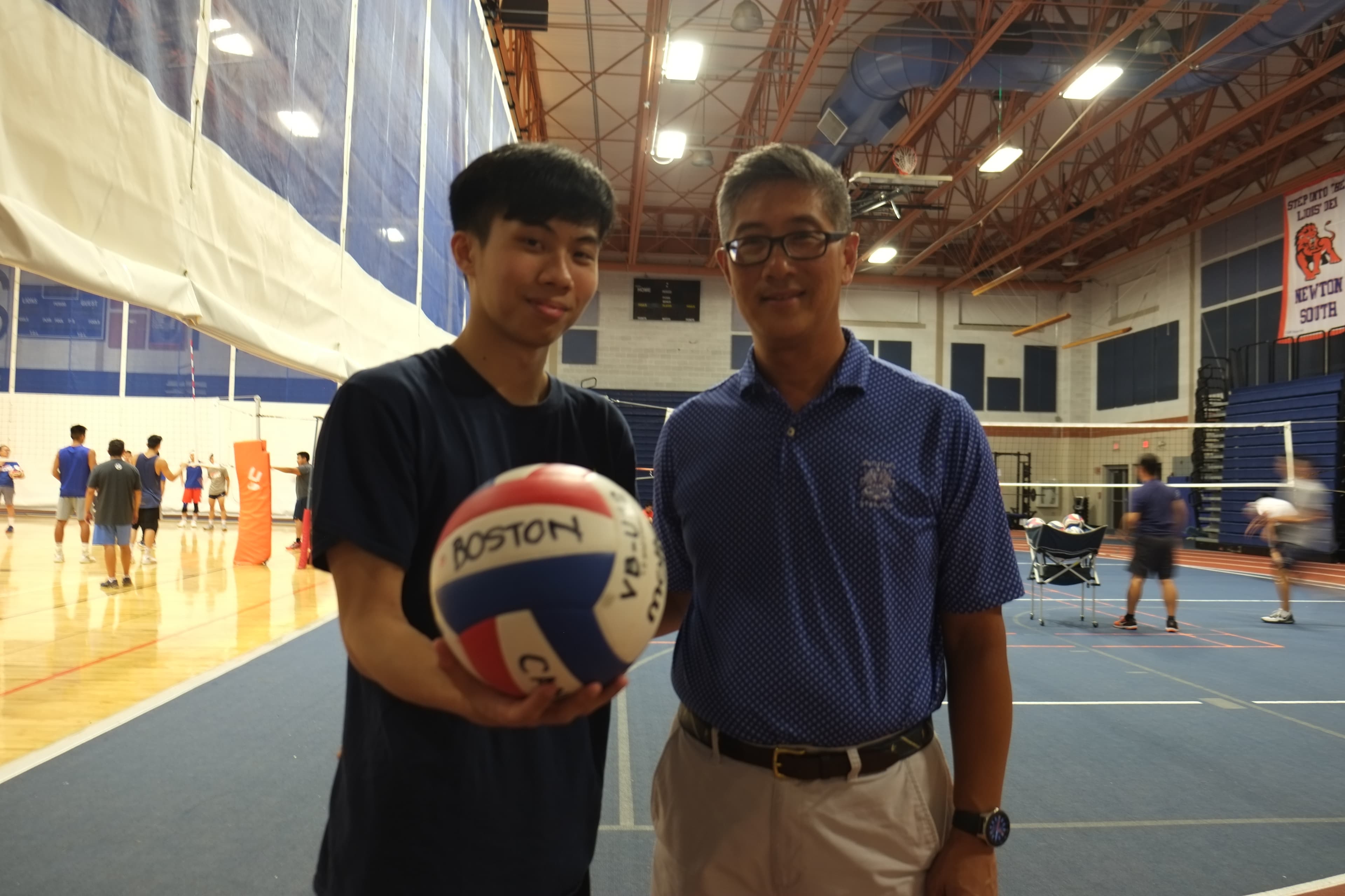 A young Asian man and older Asian man stand next to each other with a volleyball