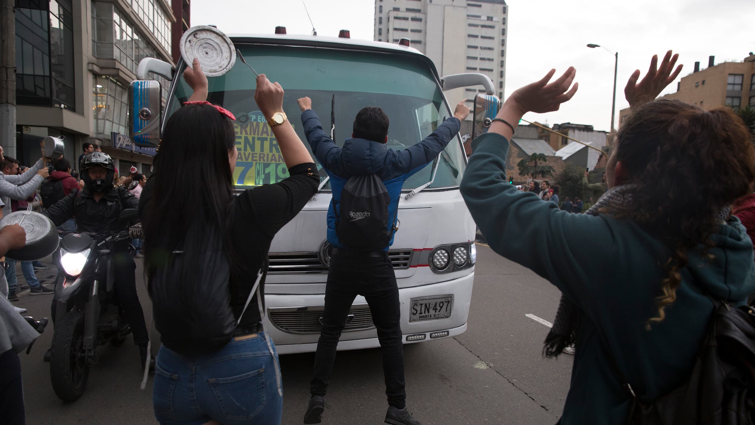 People bang on pots and pans in front of white truck