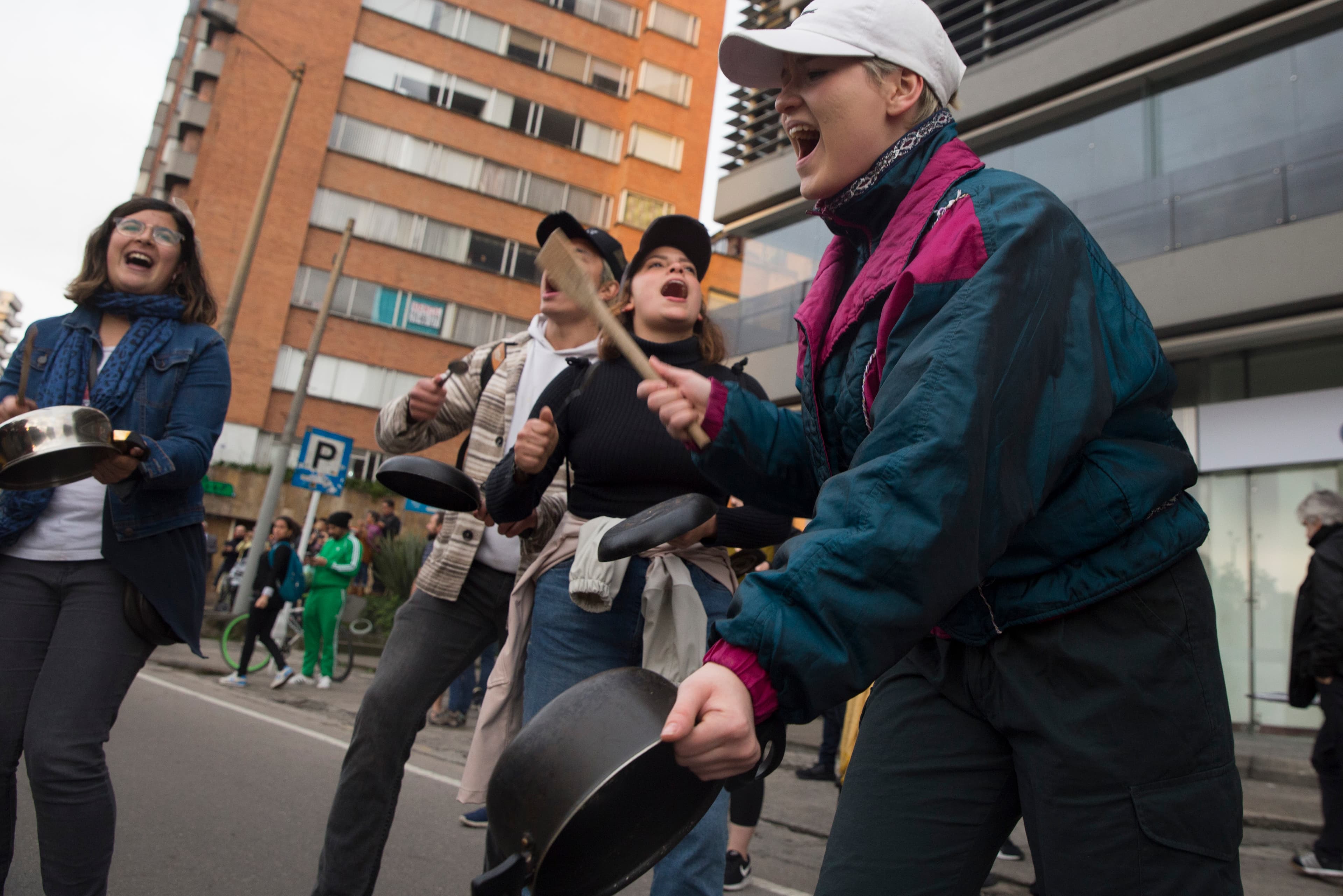 Protesters stand in a semi-circle wearing coats and bang on lids and pans