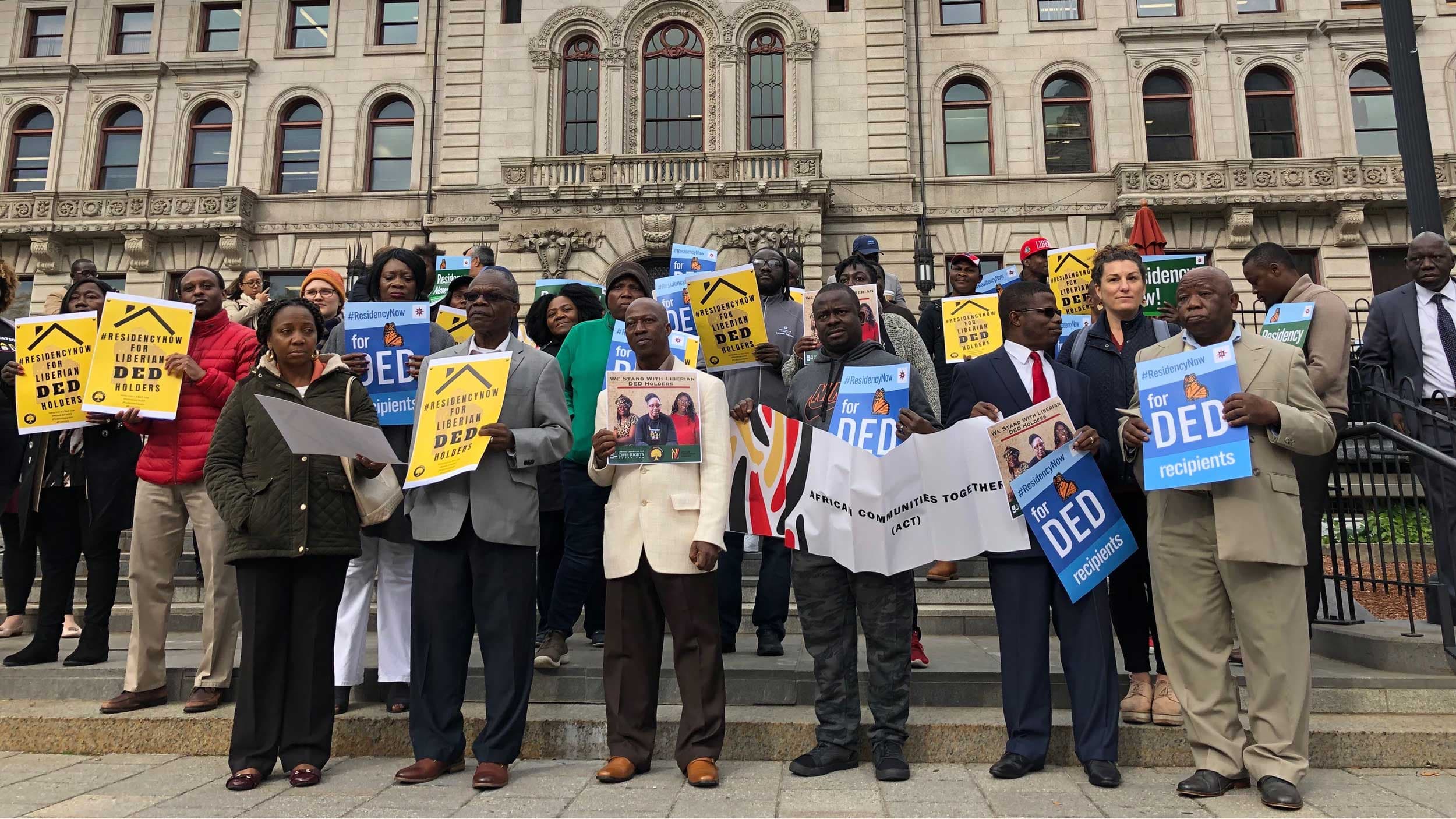 A group of people holding signs gather in front of a courthouse building