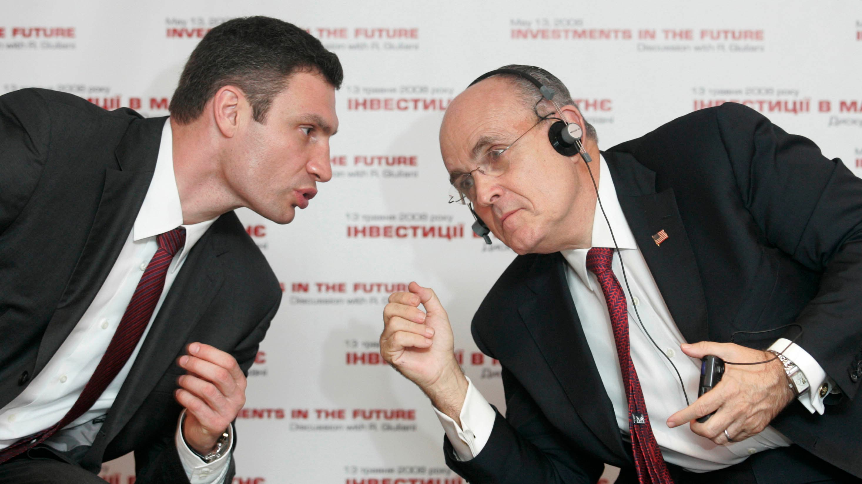 Two men in suits lean in to speak with each other