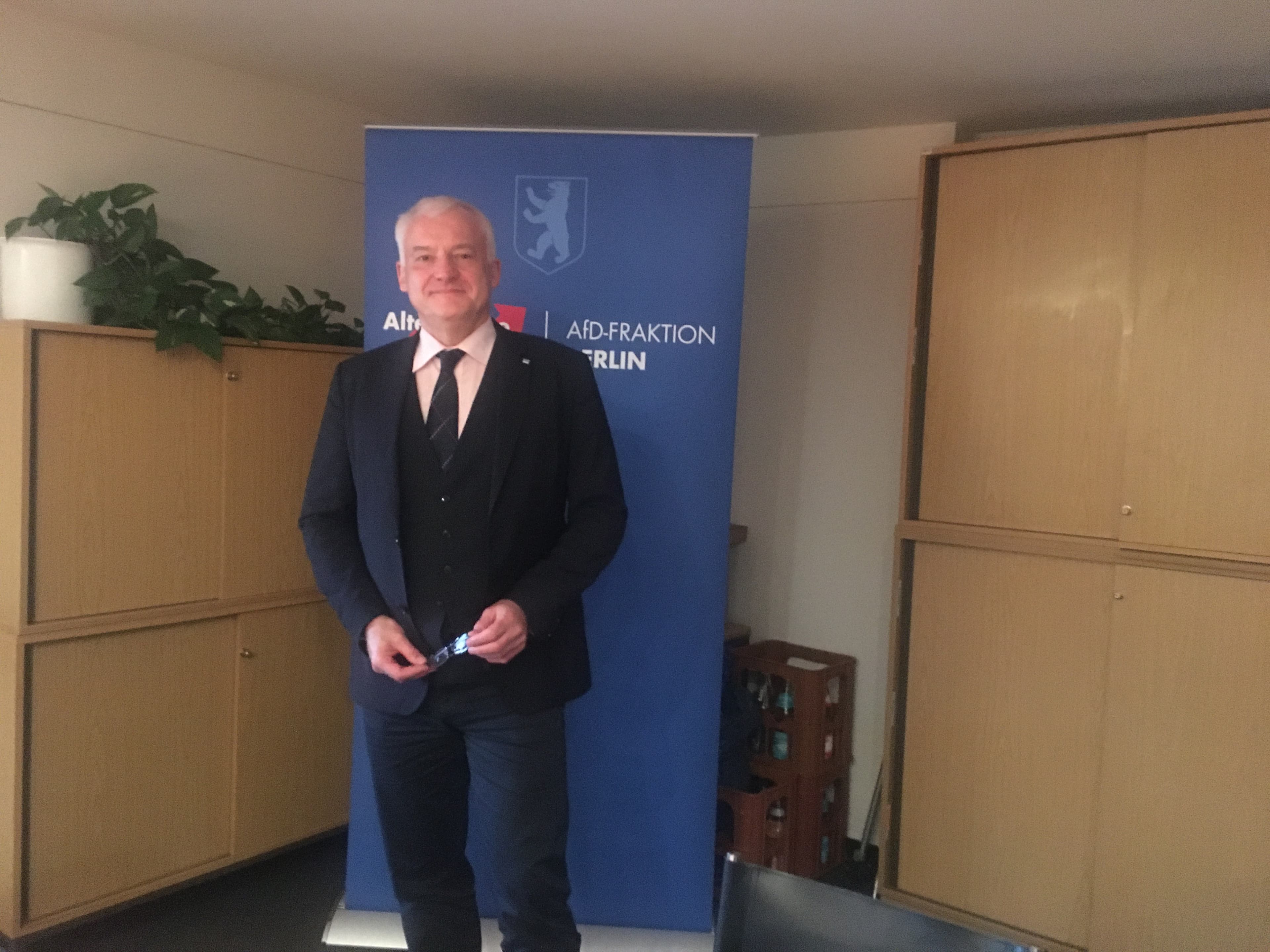 A man in a suit stands holding a pair of glasses