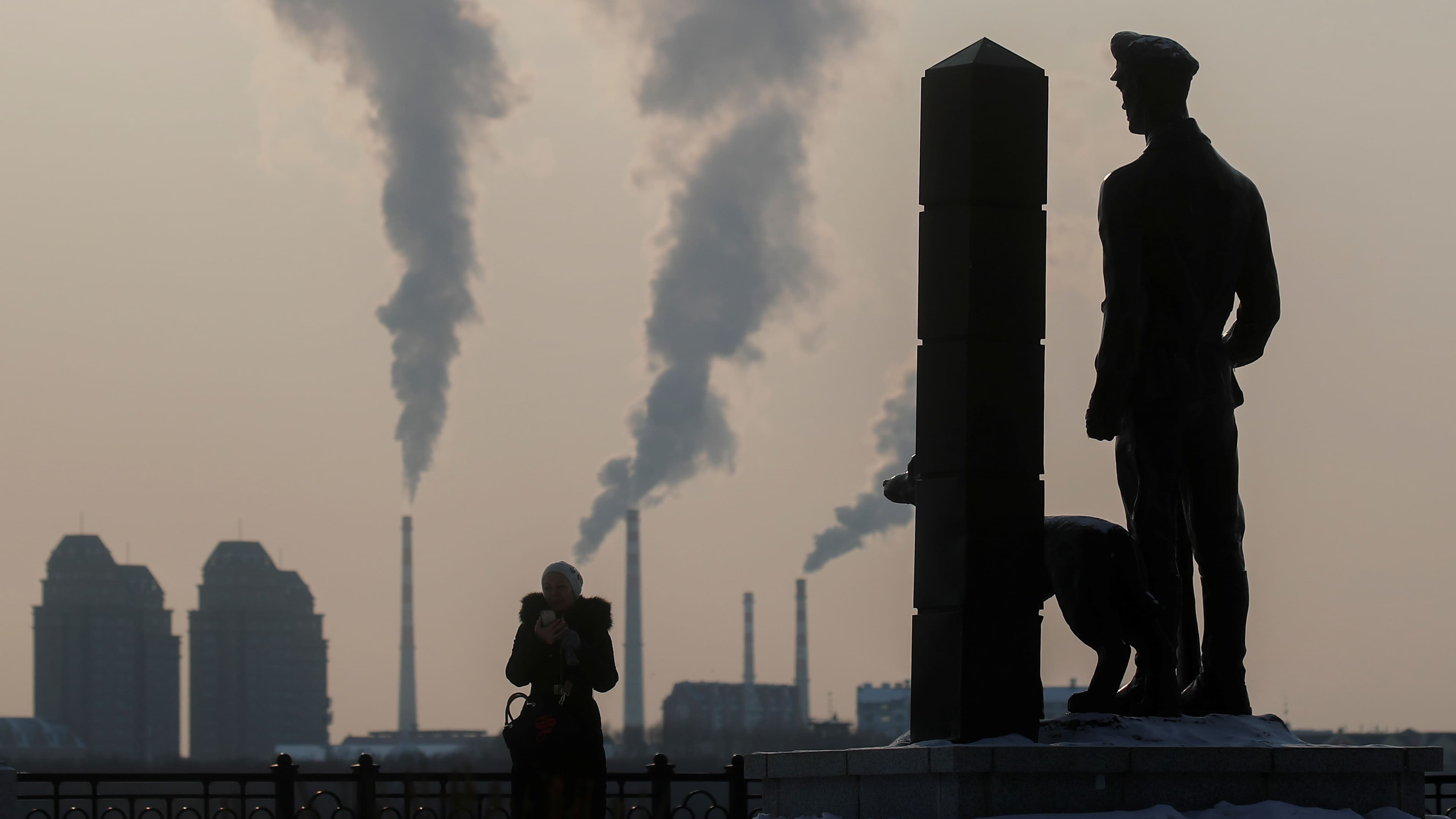 A woman stands next to a monument to a border guard with a dog, with buildings of Chinese border city Heihe seen in the background across the Amur River, in Blagoveshchensk, in Amur region, Russia, on December 1, 2019.