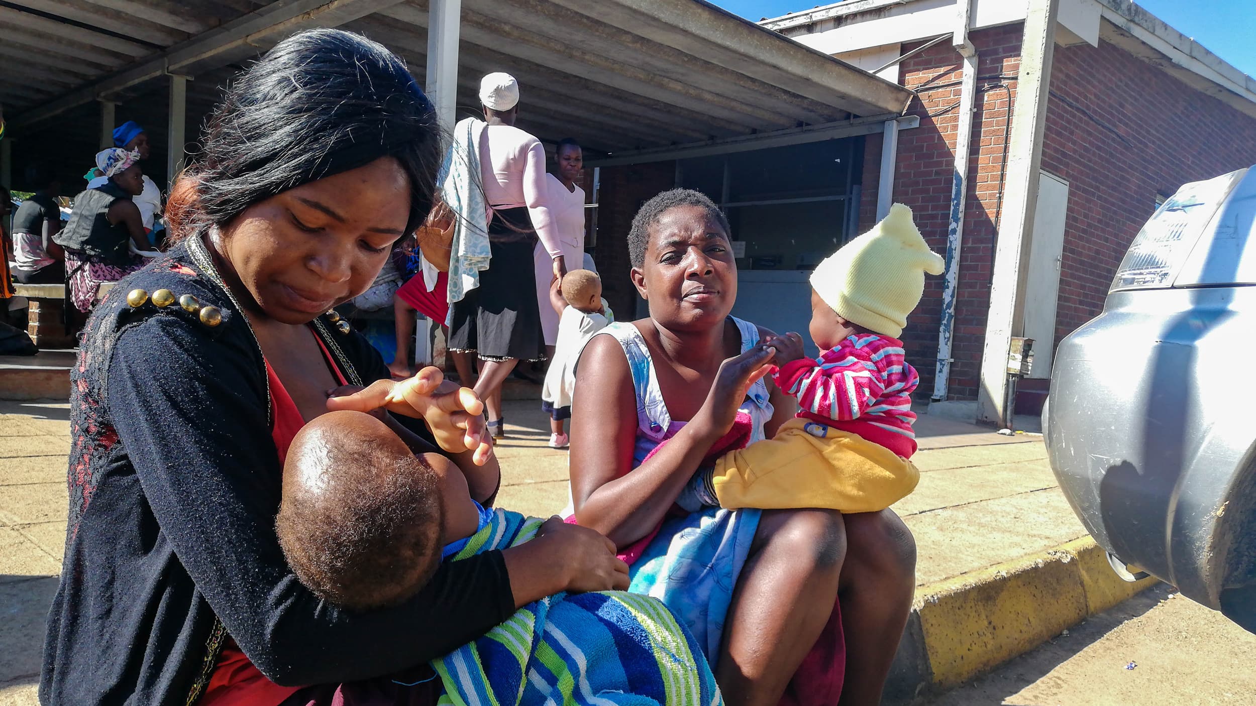 Two women sit on the curb with their infants as doctors and nurses strike at local hospital