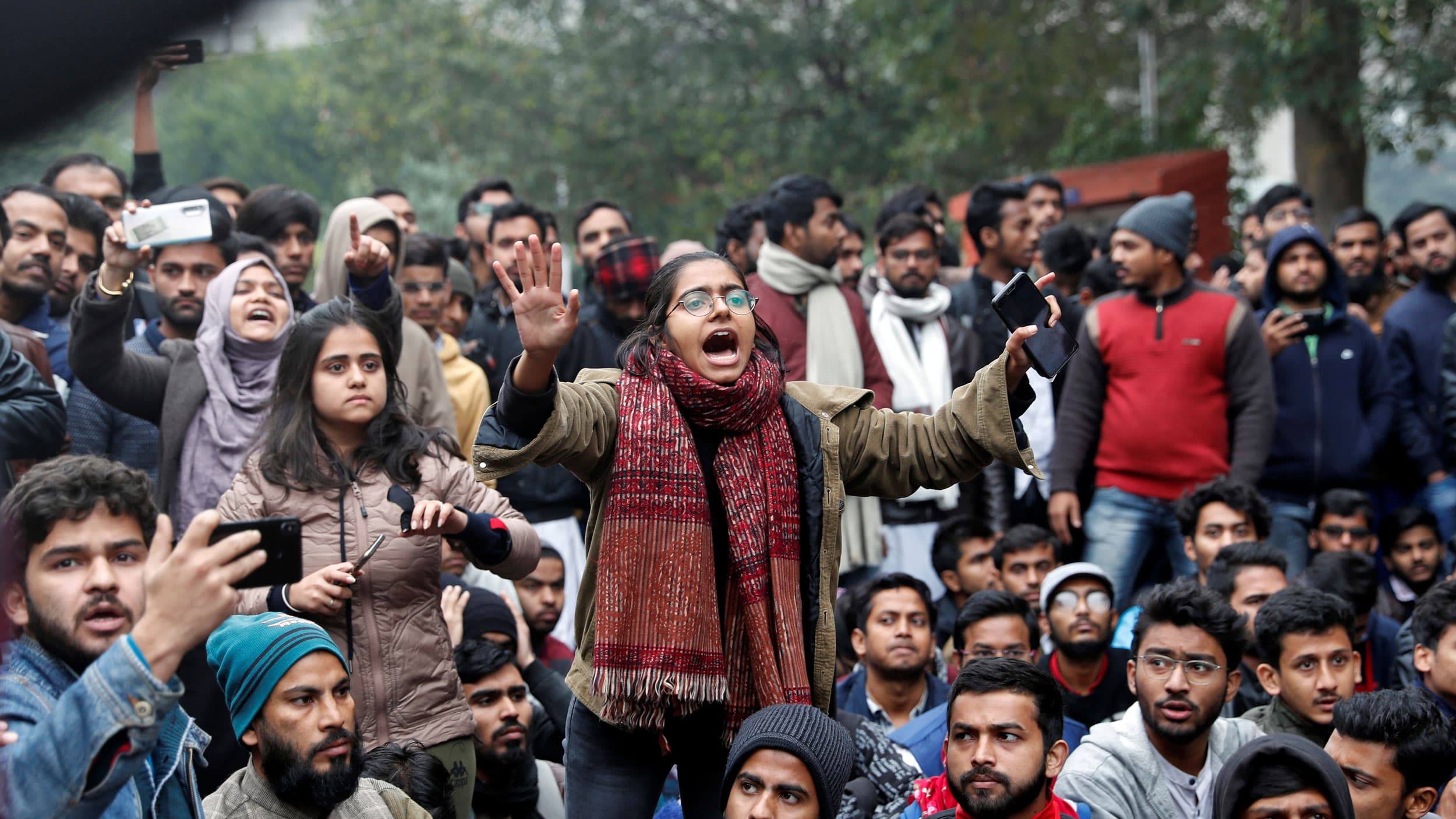 A large group of students are shown protesting with one women in the center raising her arms up.