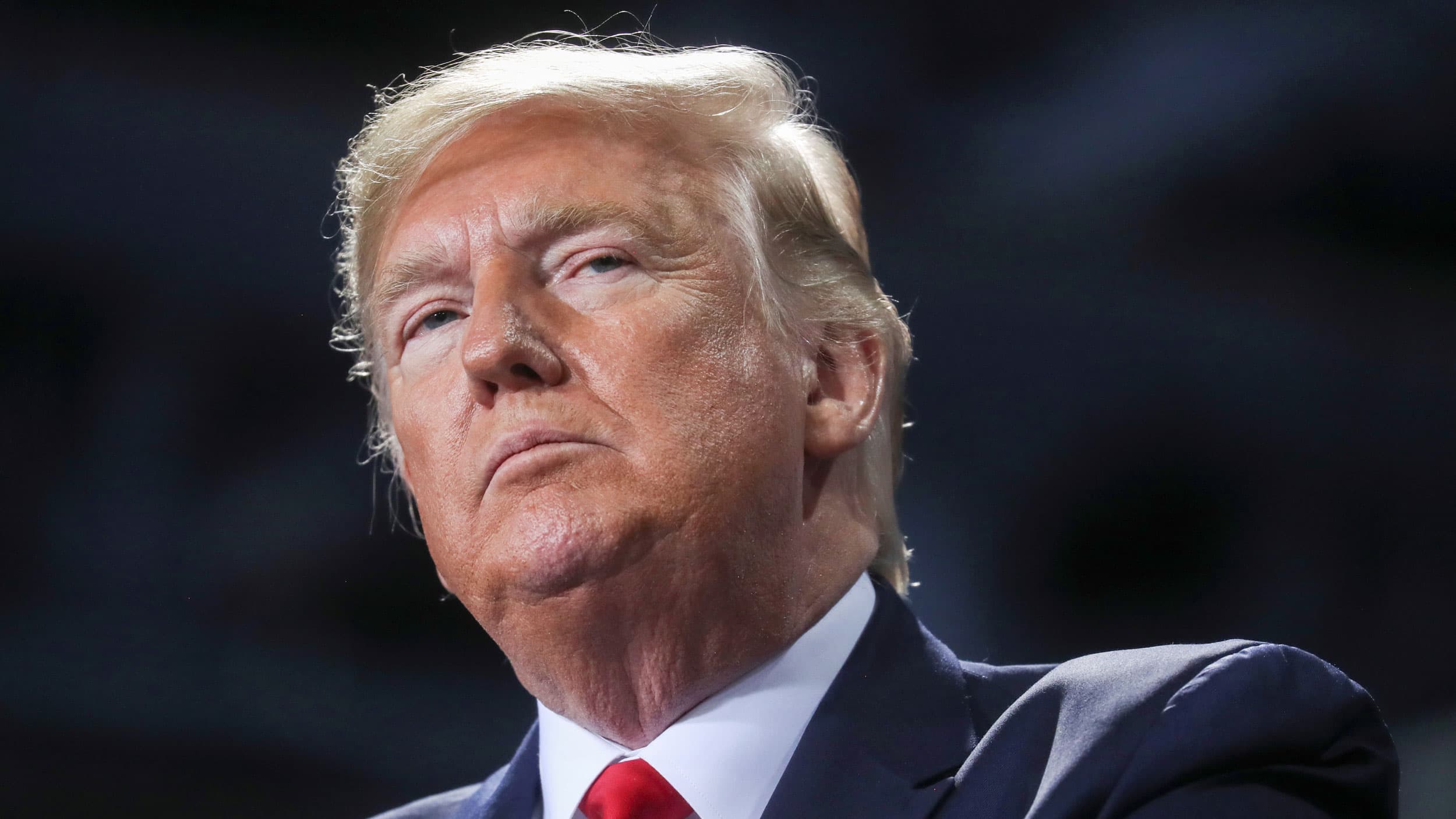 US President Donald Trump is shown in a close up photo looking off and wearing a blue suit.