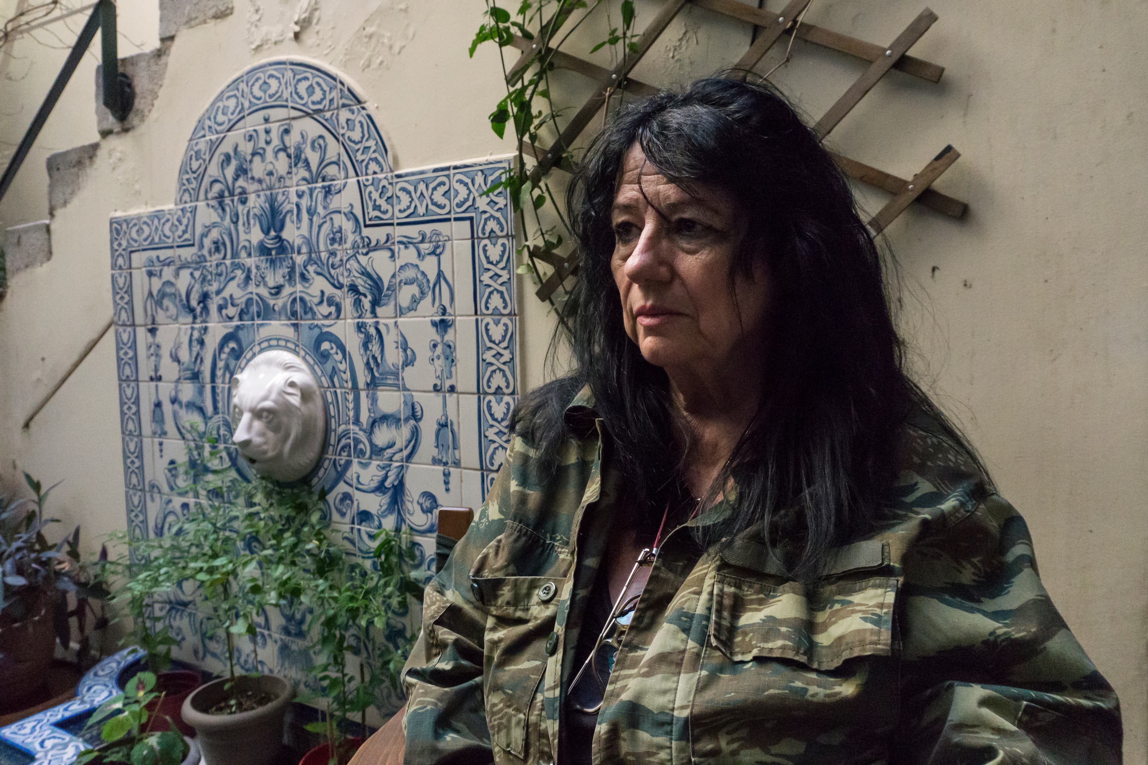 A woman with dark hair and army jacket stands near a tiled fountain