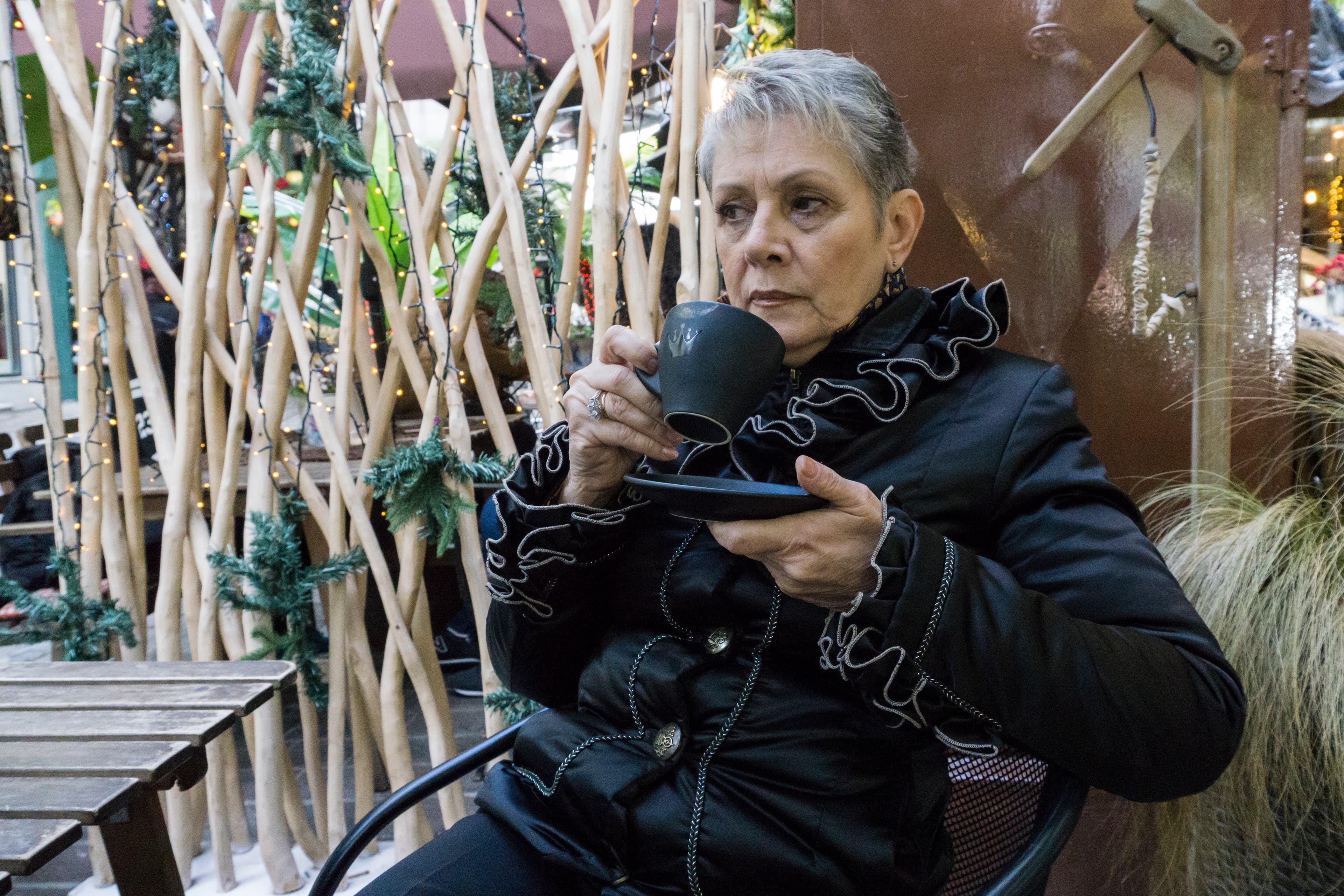 Avrilia Kosmaidou sits and sips from a cup wearing a black jacket