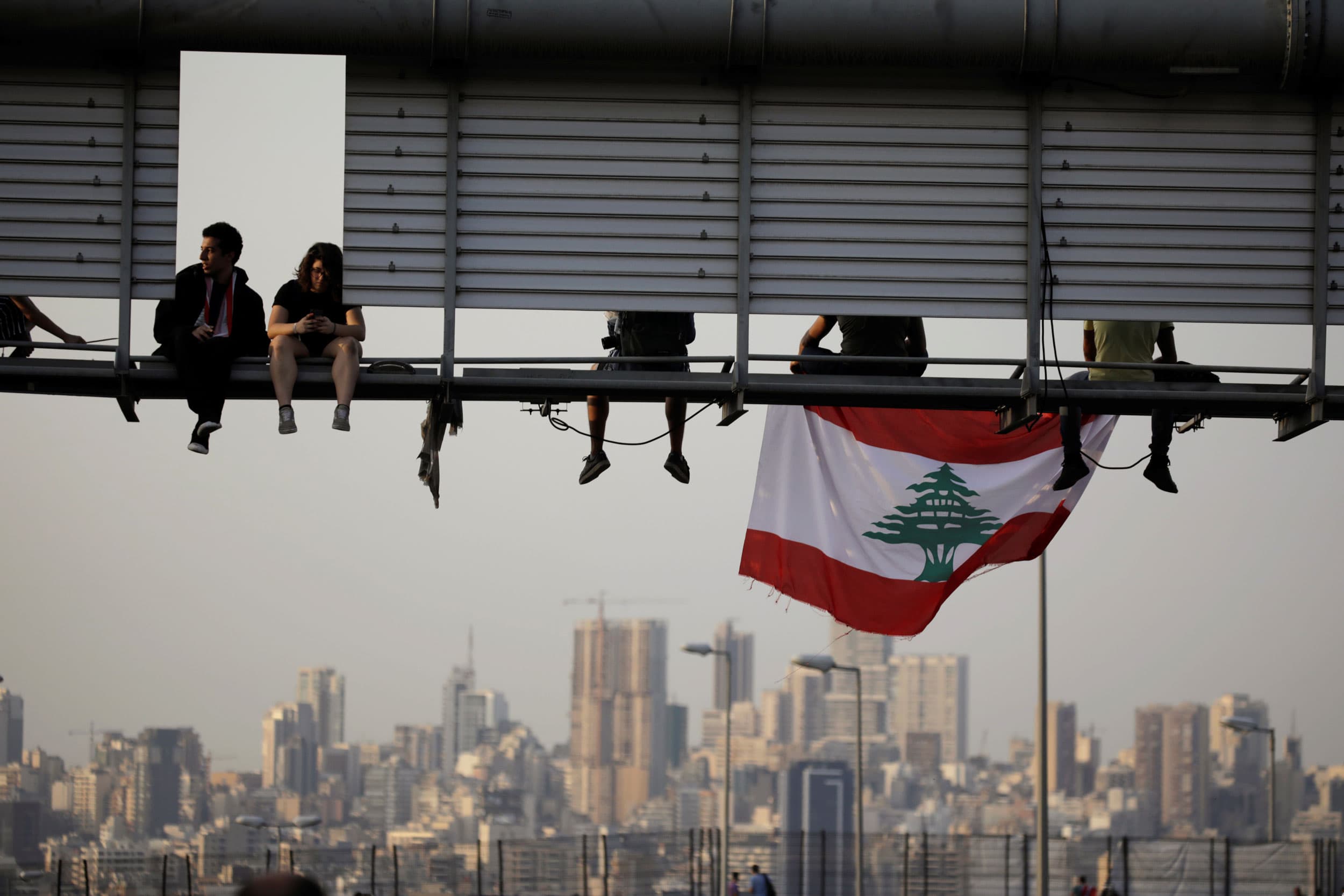 Several protesters are shown sitting on road sign spanning across above the road.