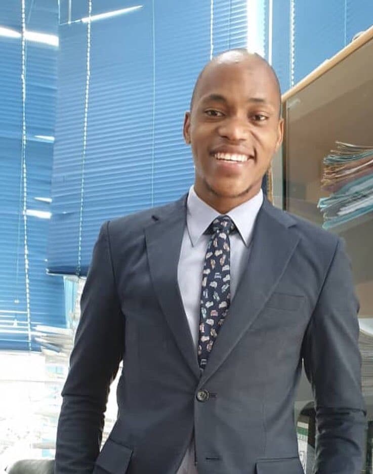 A young man smiles wearing a suit and tie