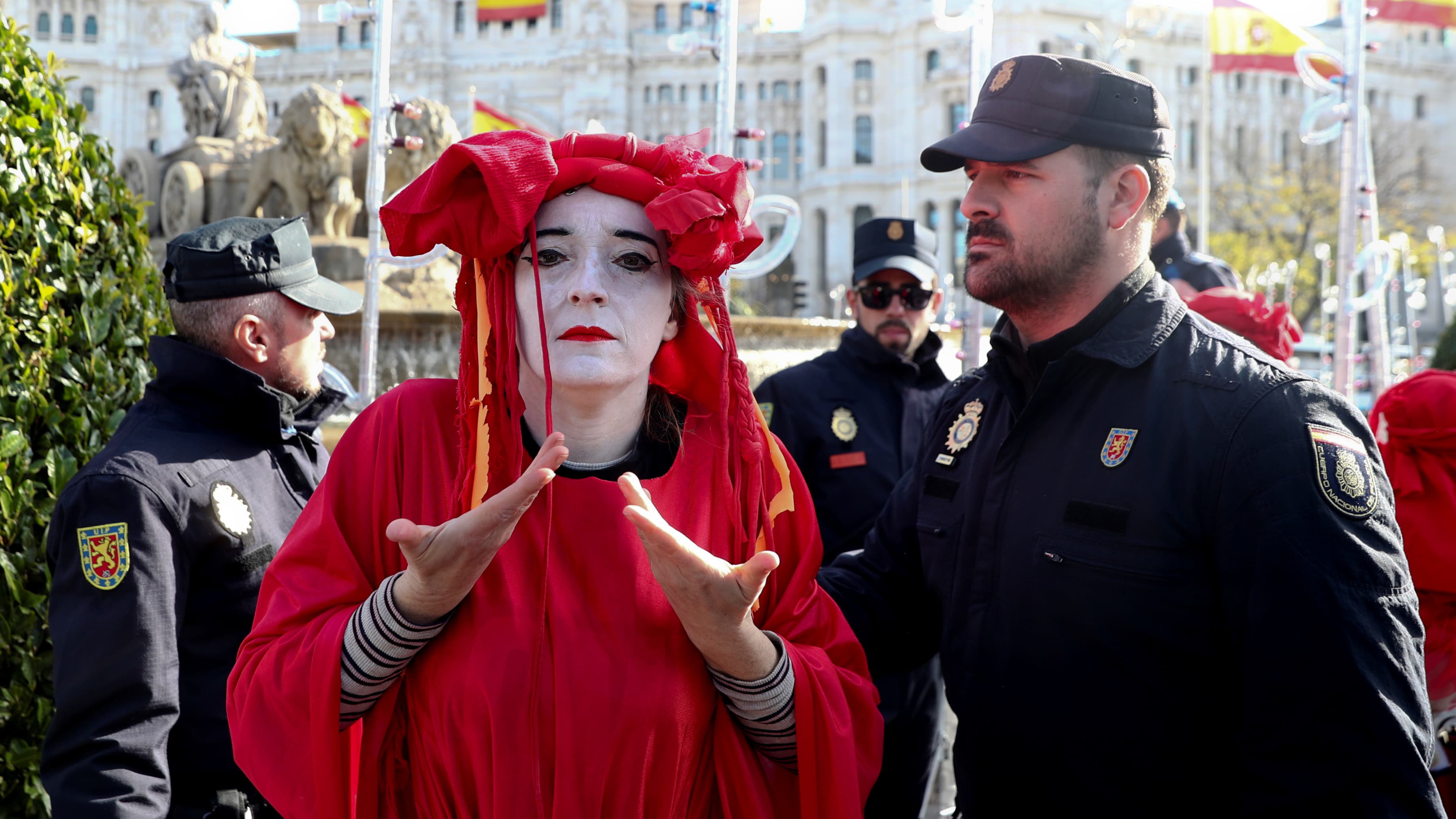 A person with white face paint and red robes stands near man in black uniform