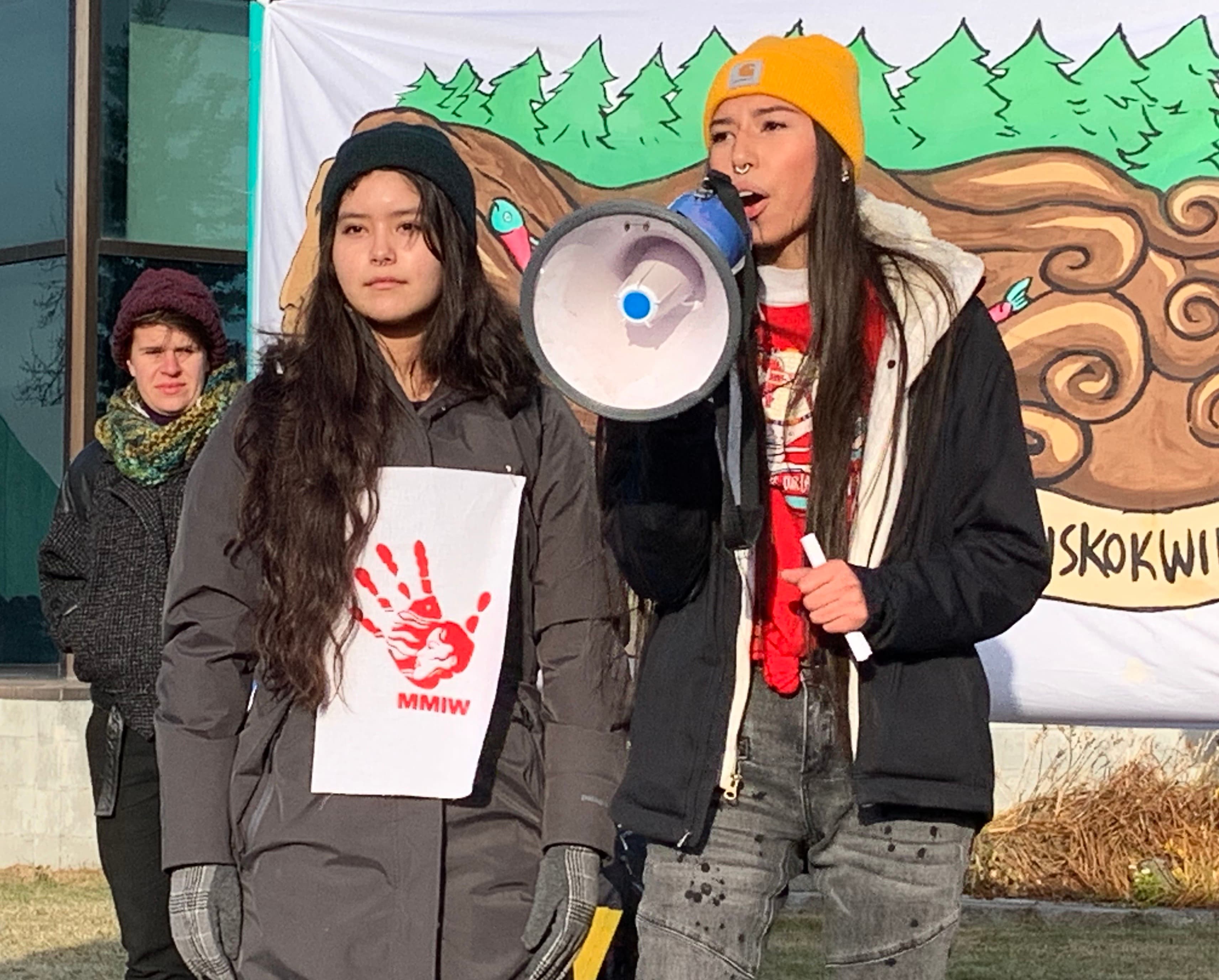 Two young women speak with a megaphone to announce climate emergency