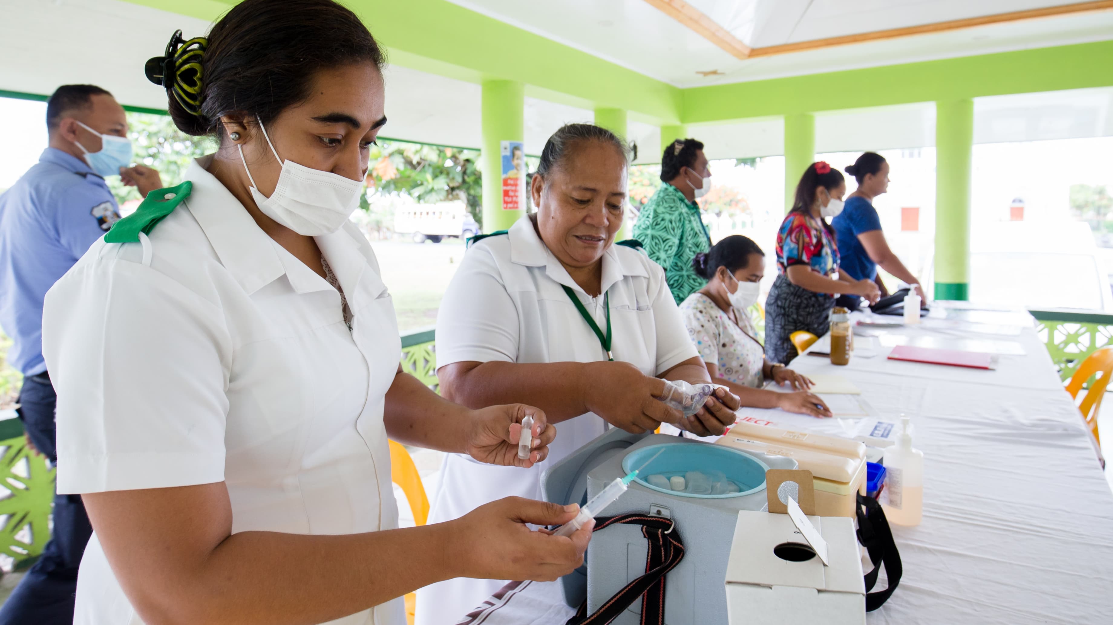 A nurse wears a white face mask as she holds a syringe in her hand