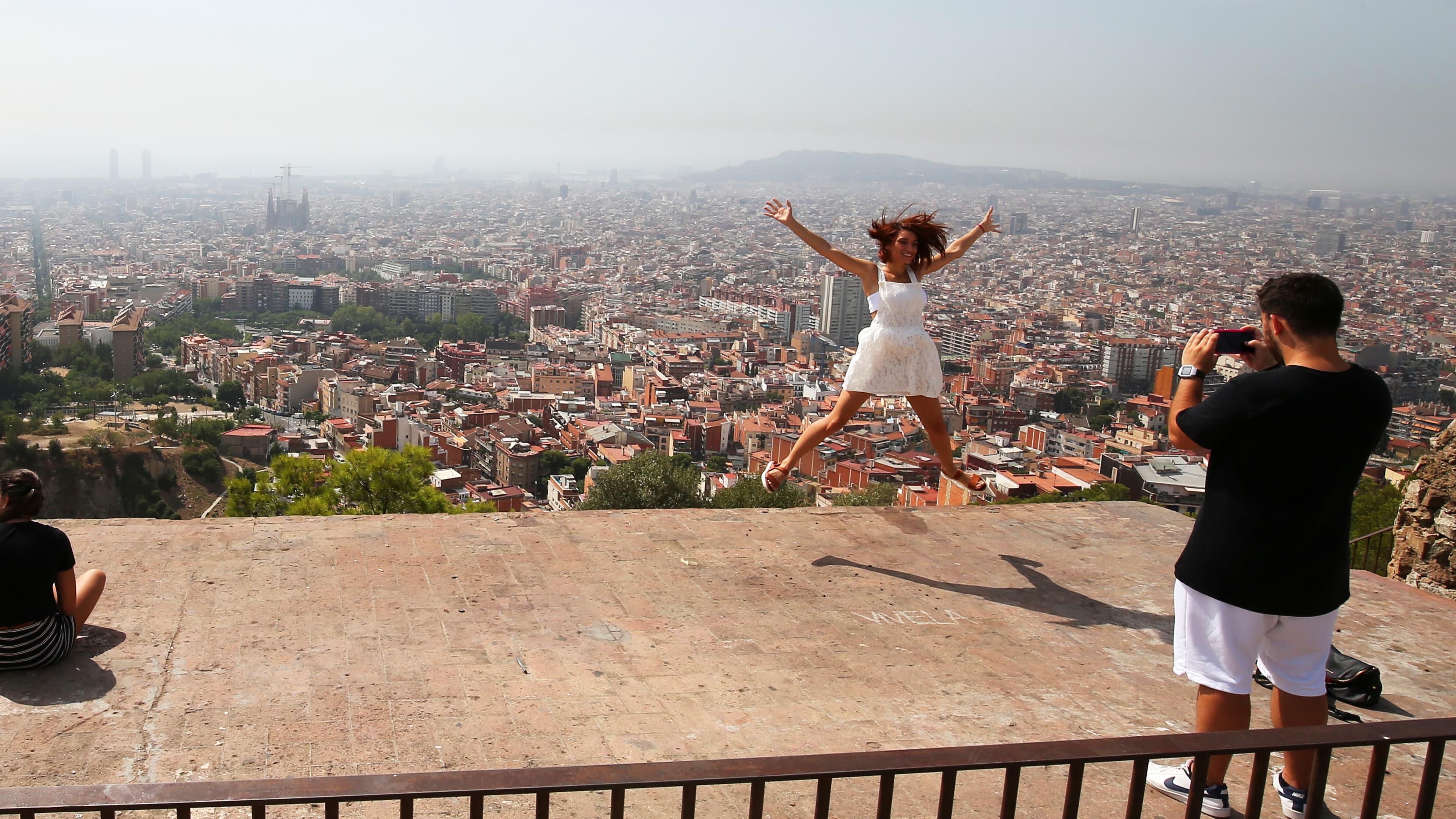 A tourist leaps in the air with a backdrop of the skyline of Barcelona
