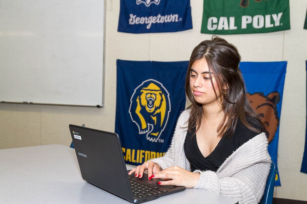 A young woman sits in front of a laptop typing.