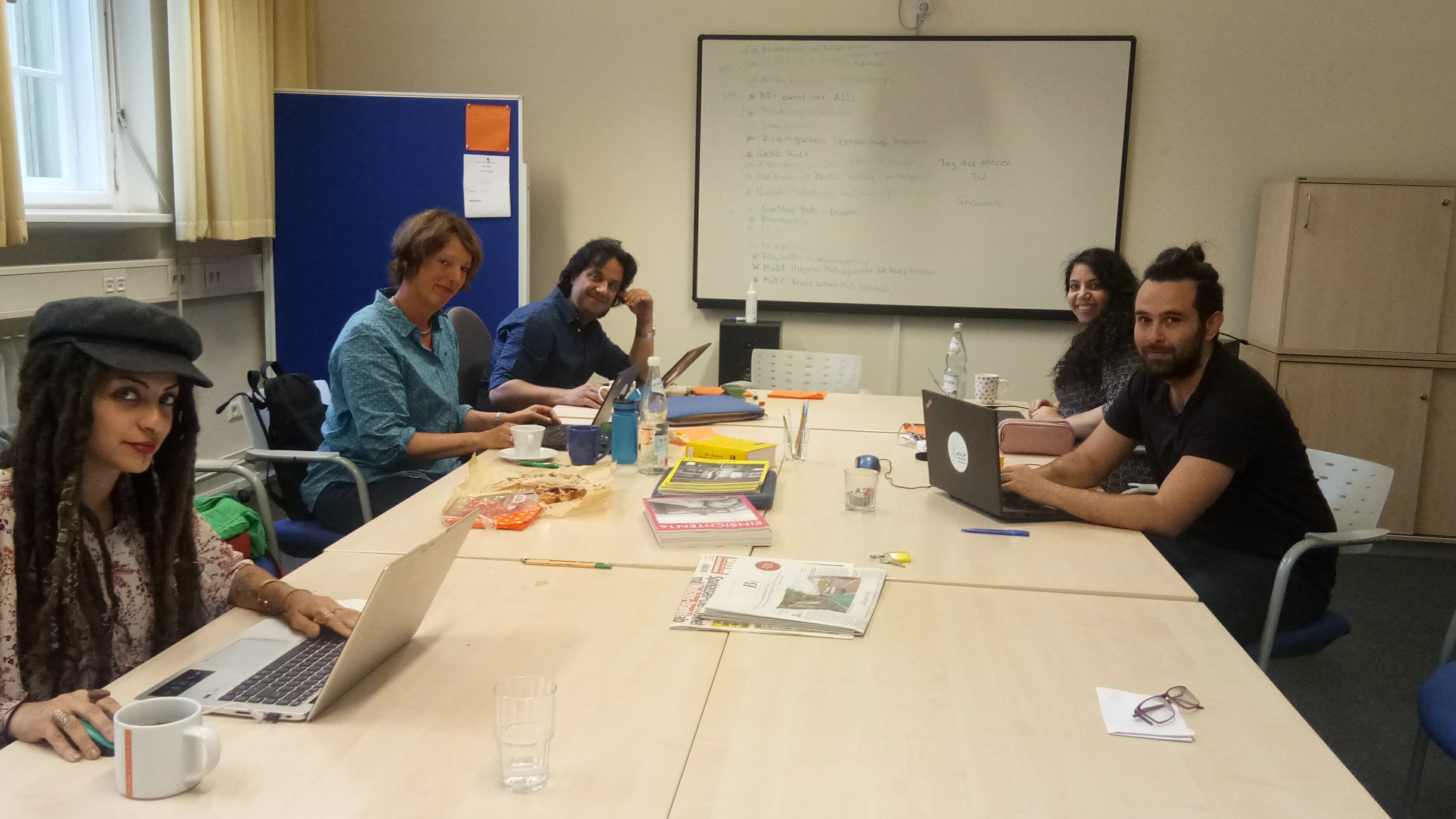 A group of people sit around a table with laptops.