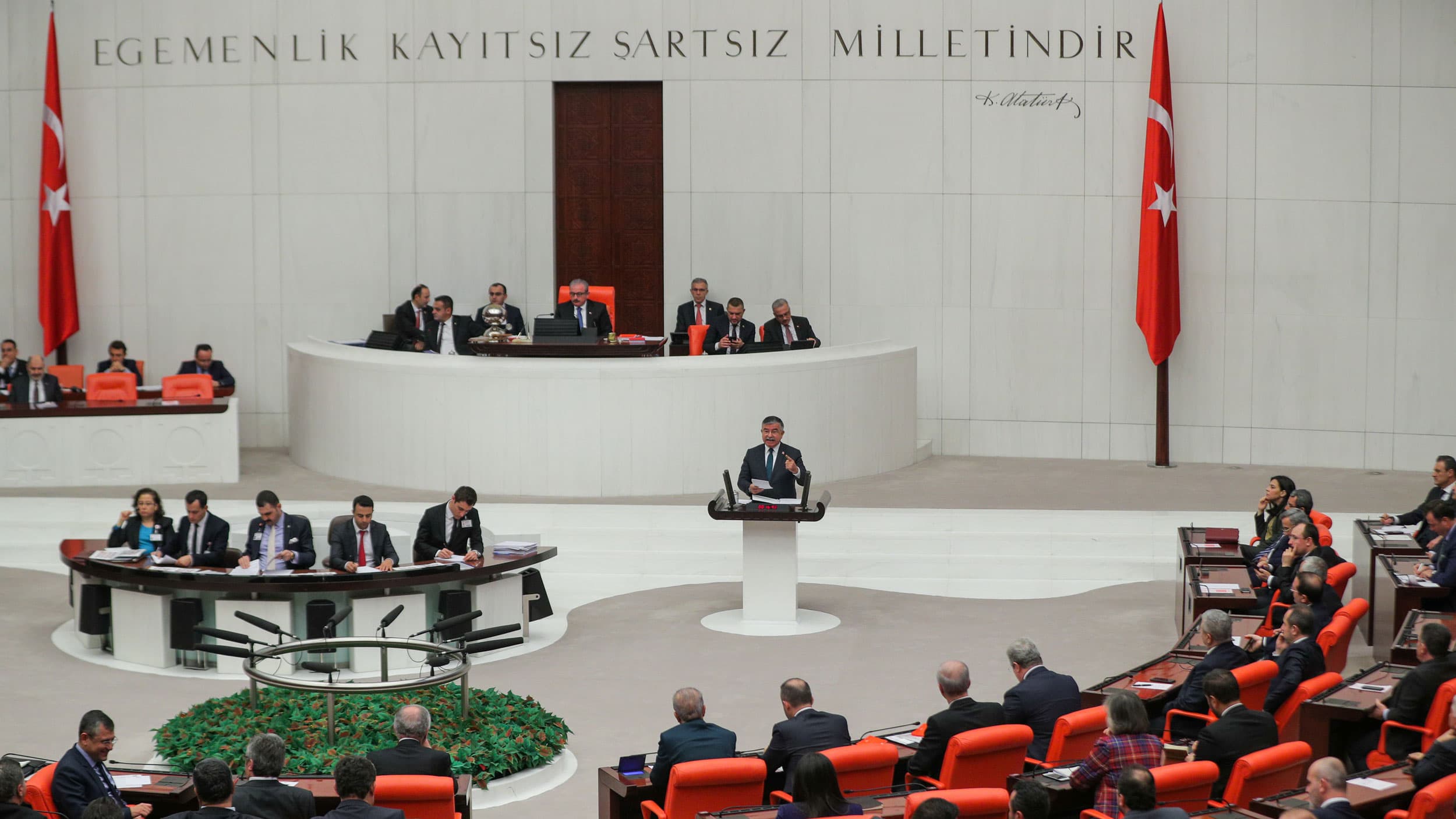 A man at a podium with groups of seated people around him
