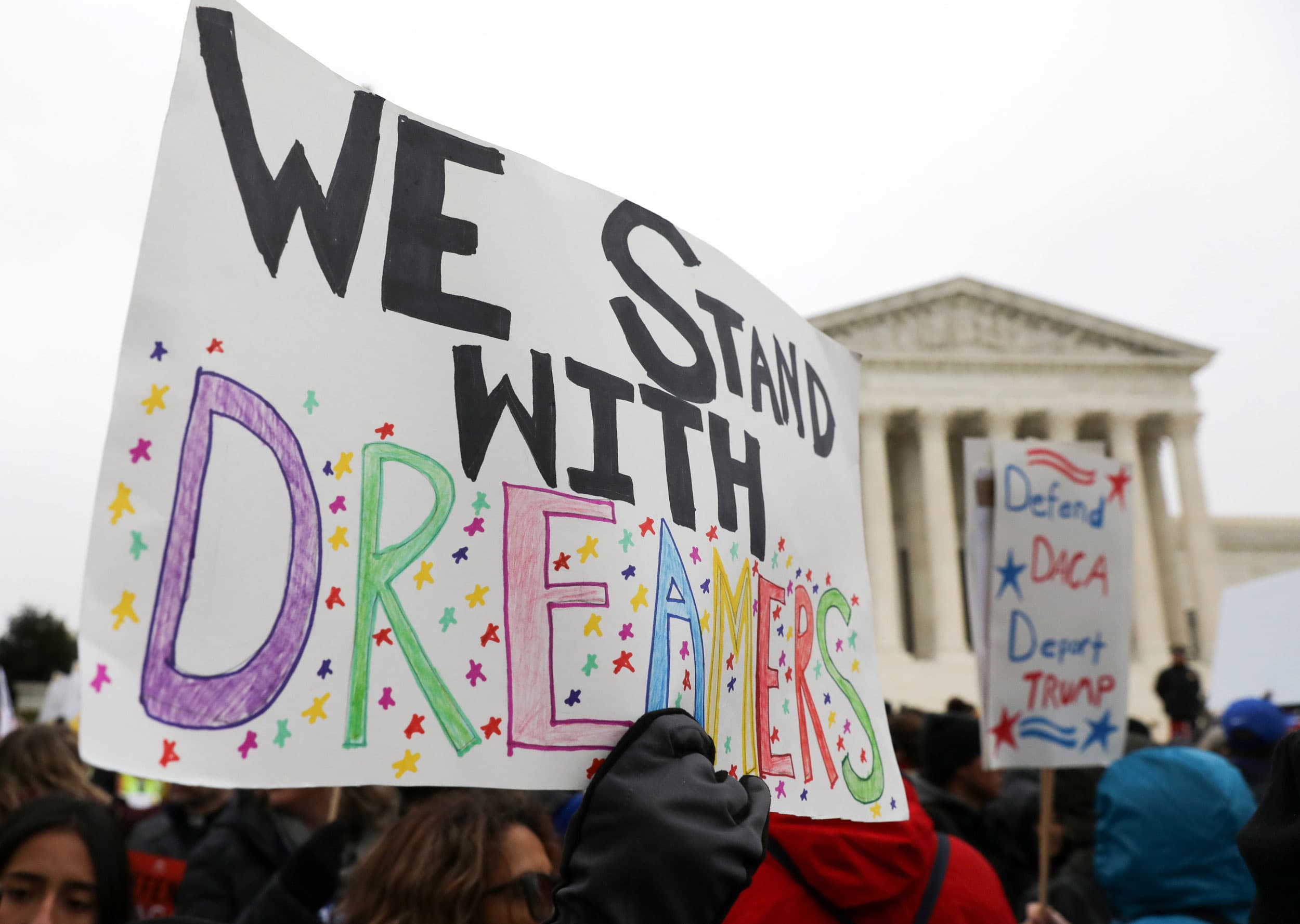 A group of demonstrators are standing an carrying signs with one that has, 