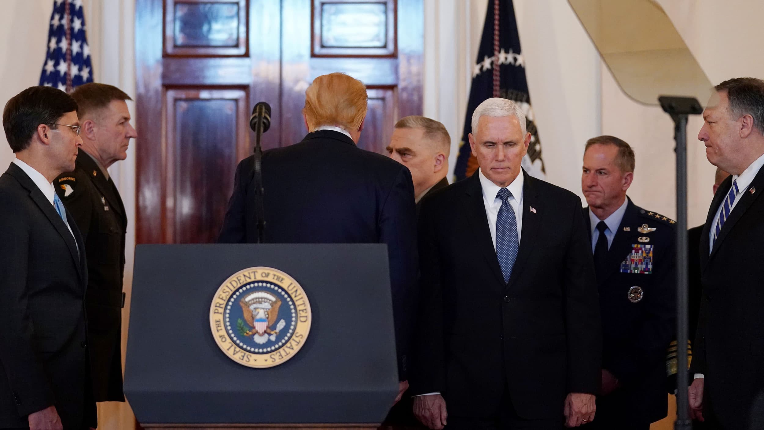President Donald Trump departs from a podium, flanked by several officials