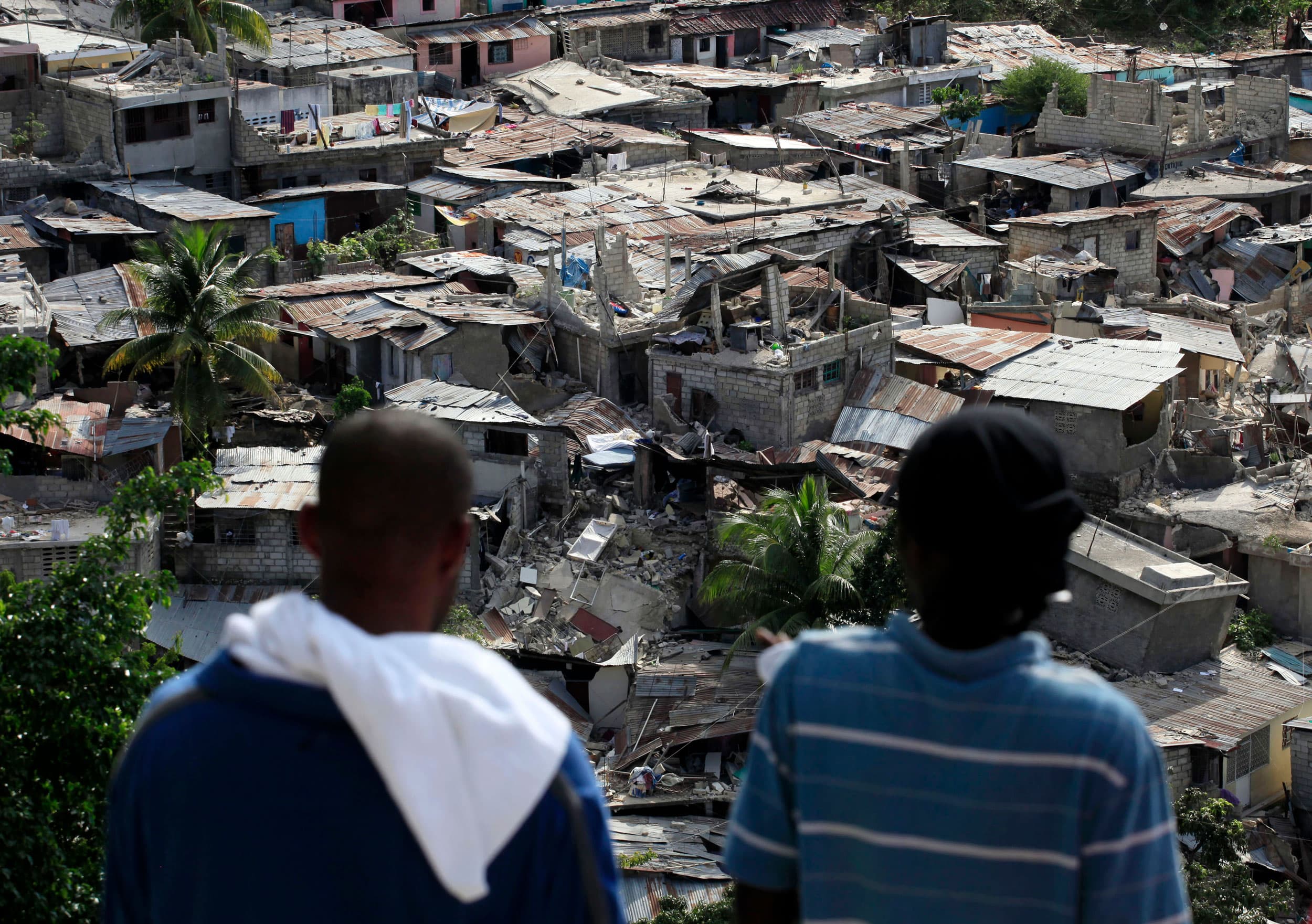 Two people are pictured from behind overlooking a scene of devastation