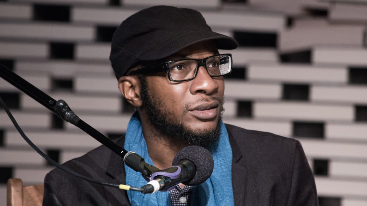 a man wearing glasses and a hat sits behind a microphone