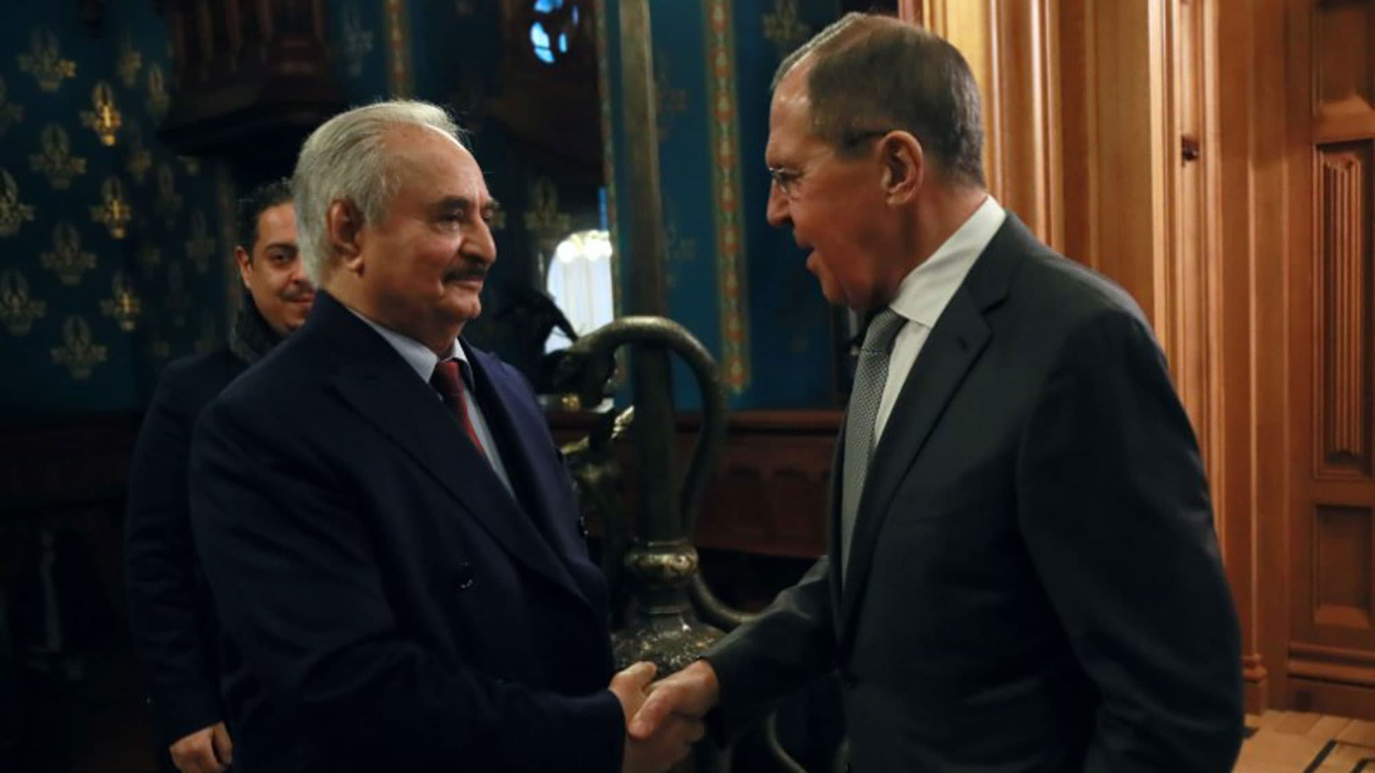 Khalifa Haftar and Russian Foreign Minister Sergei Lavrov, both wearing suits, are shown shaking hands.