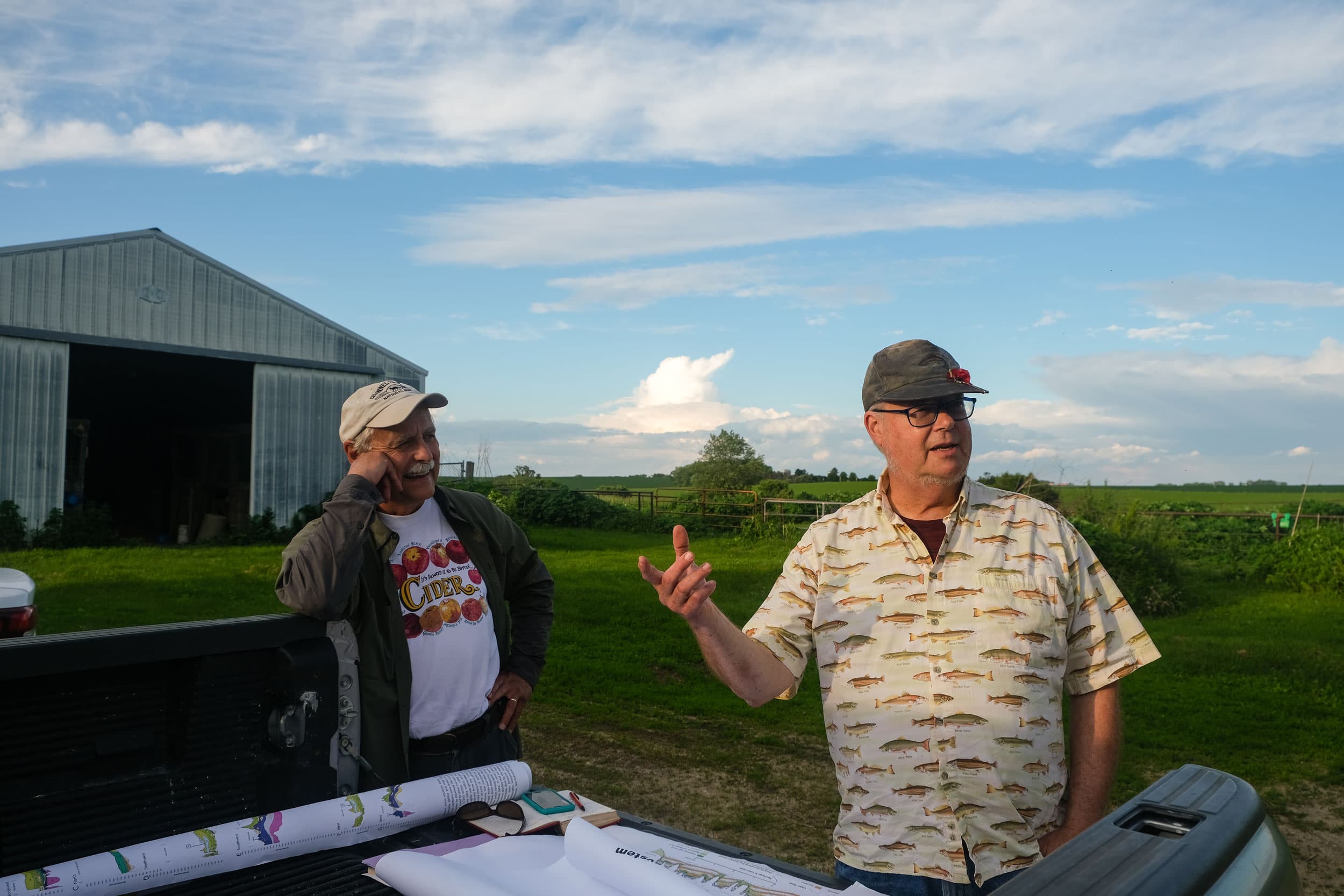 Two men are shown standing at the back of a pick-up truck with barn in the backgroud.