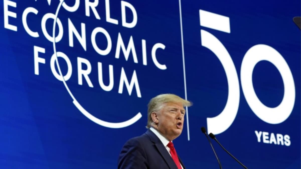 A man speaks into a microphone in front of a blue wall.