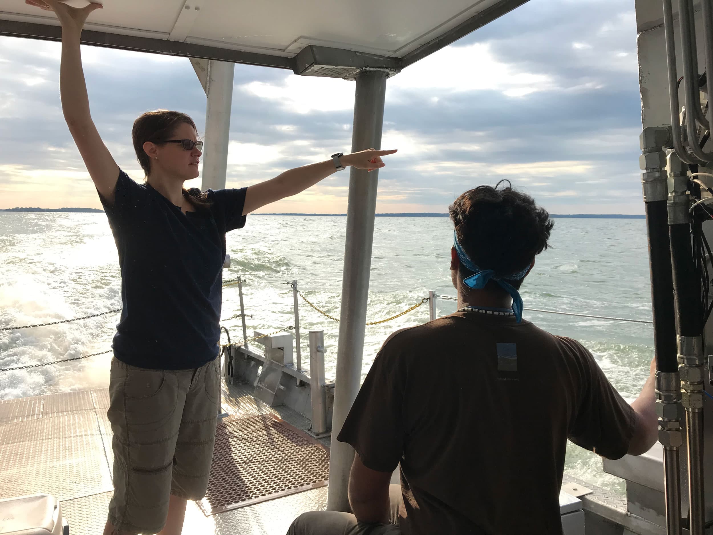 A woman is shown standing an pointing out to water on a sunny day.