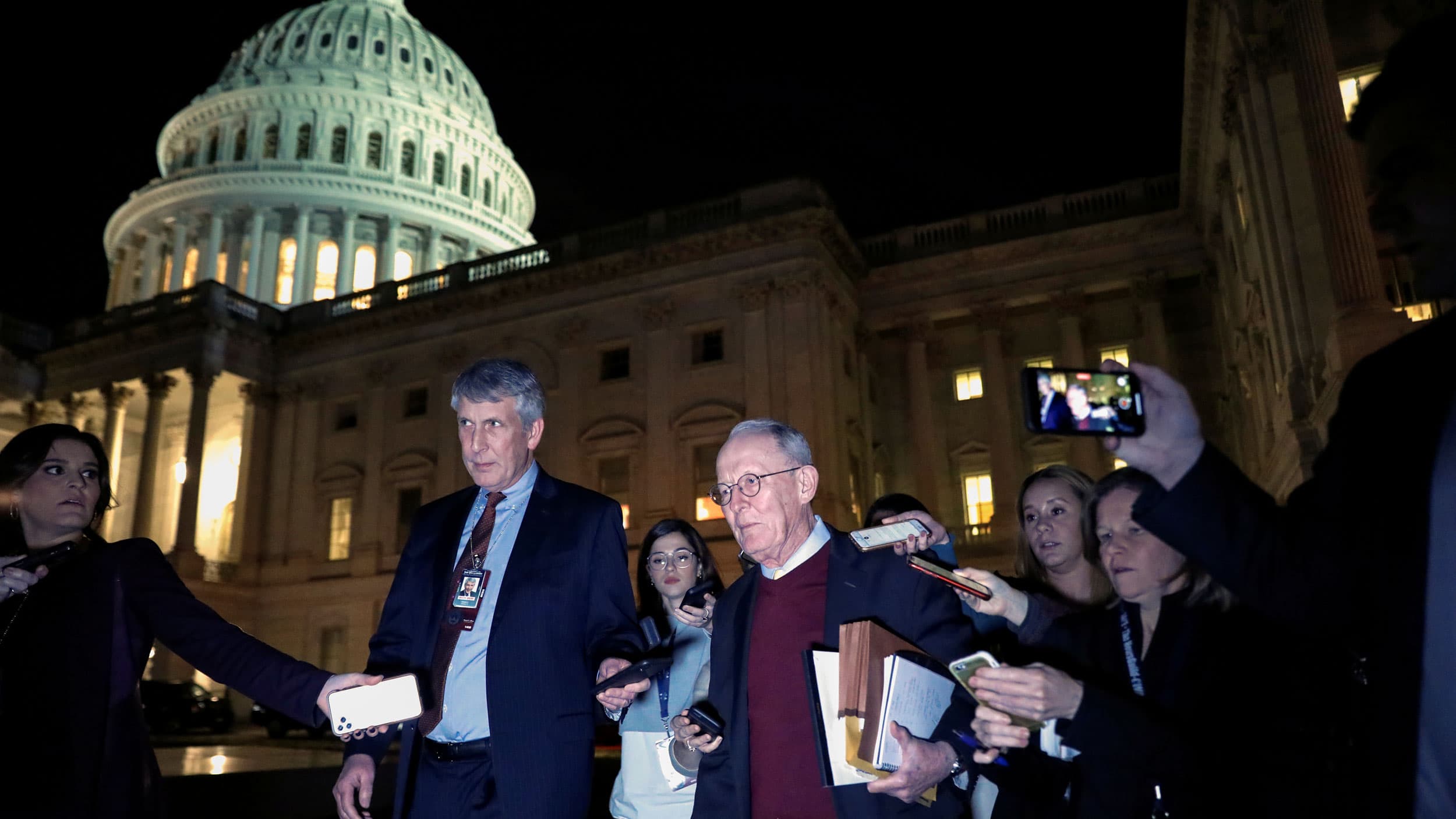 US Senator Lamar Alexander is shown outside in the dark evening hours with the glow of the Capitol building dome behind him.