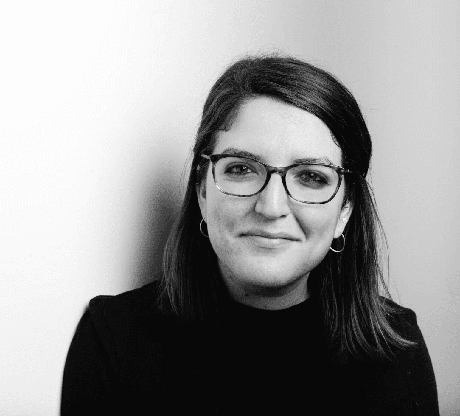 A woman wearing a dark sweater and glasses looks at the camera.