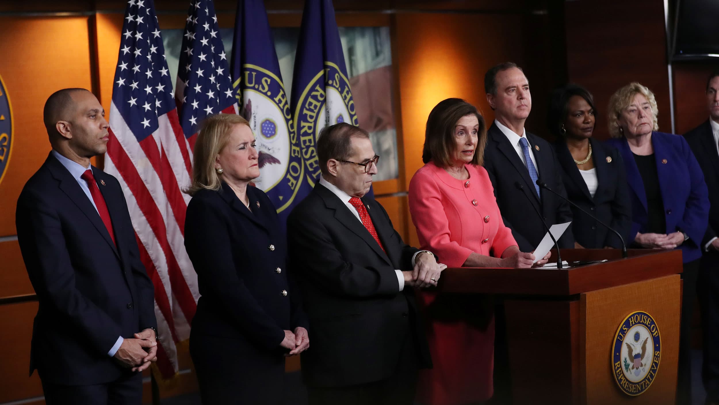 Several lawmakers stand behind a podium with flags in the background