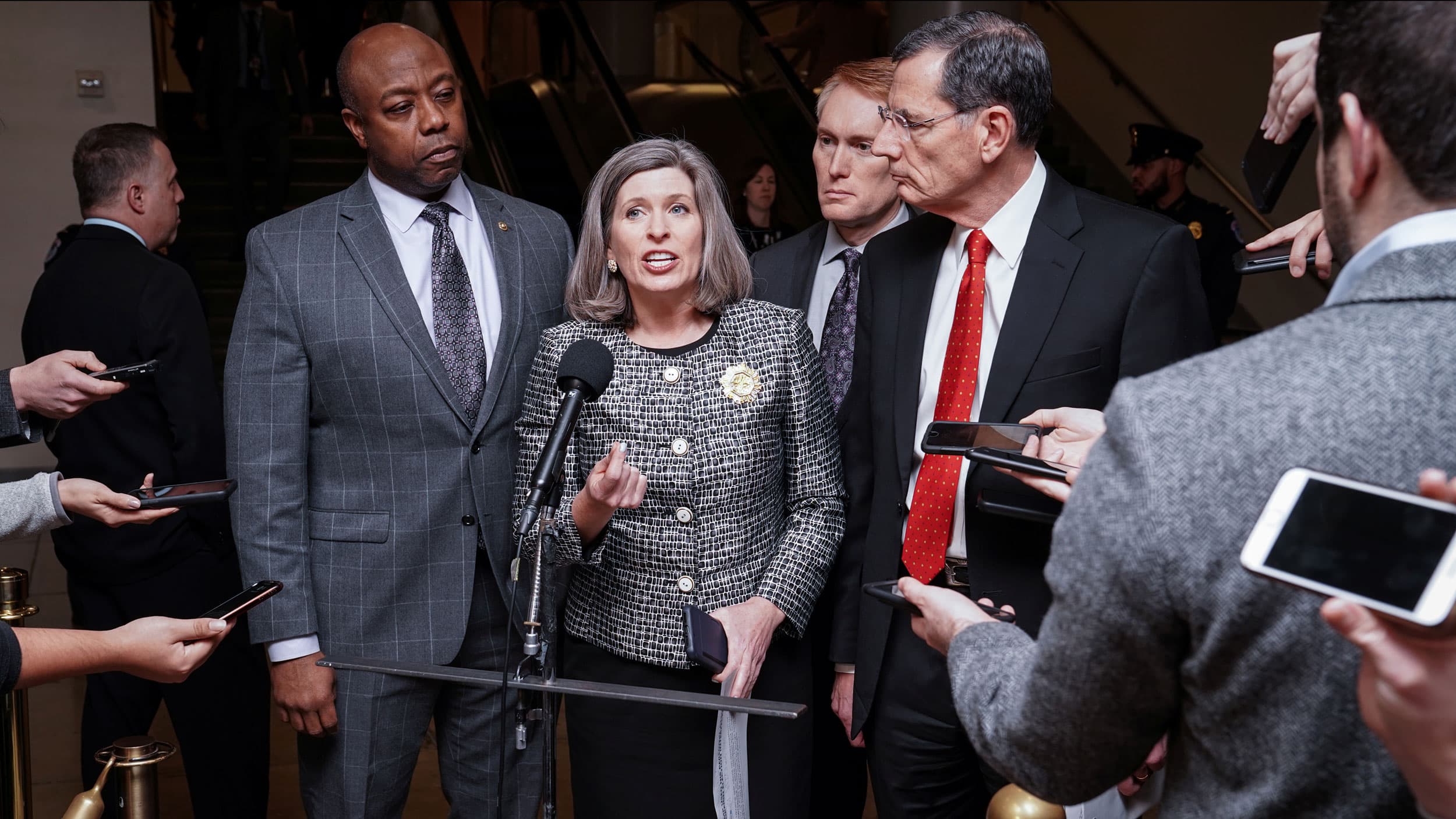 A woman speaks surrounded by men