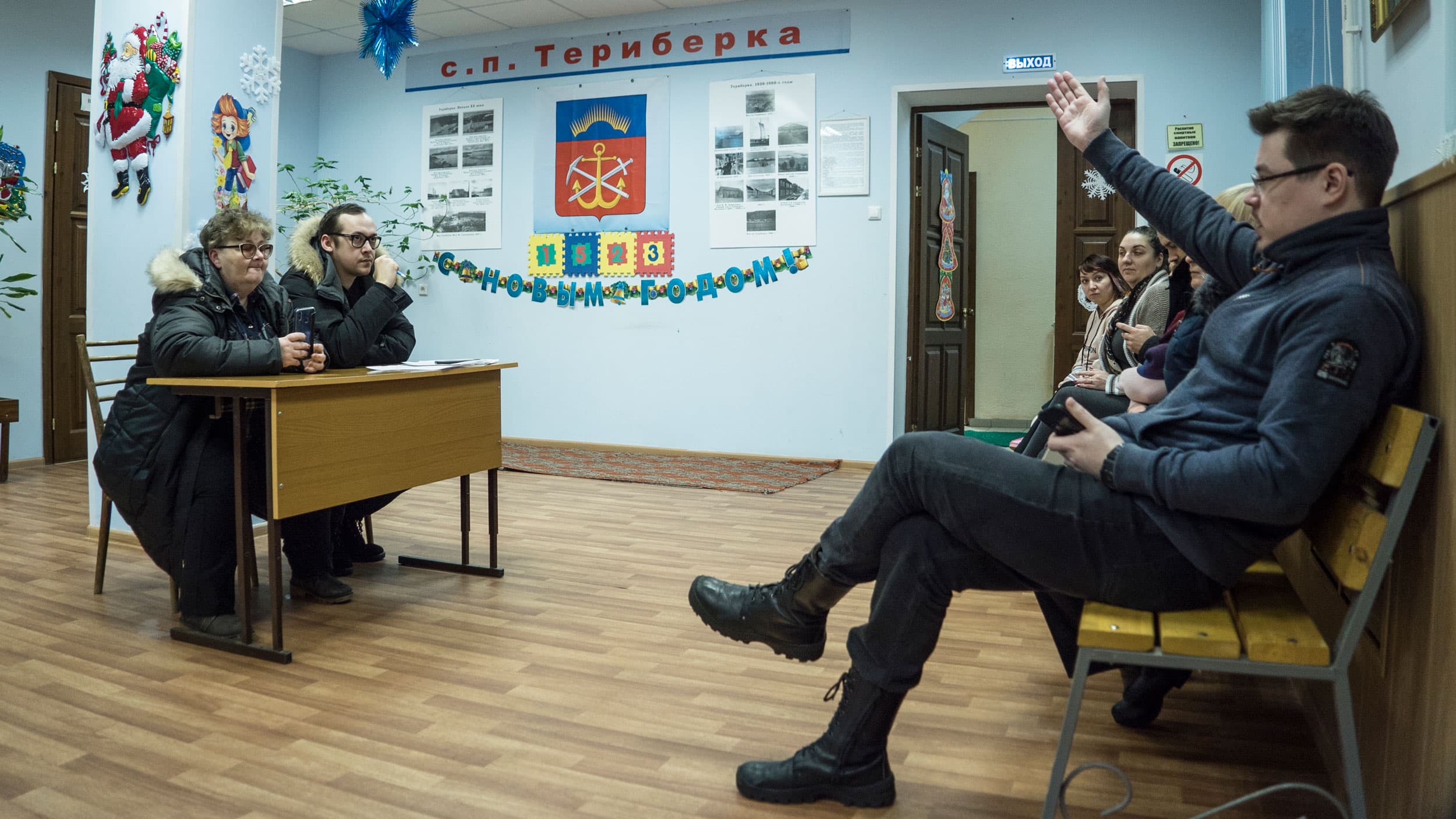 A man and a woman are shown sitting at a small desk with a row of people across from them.