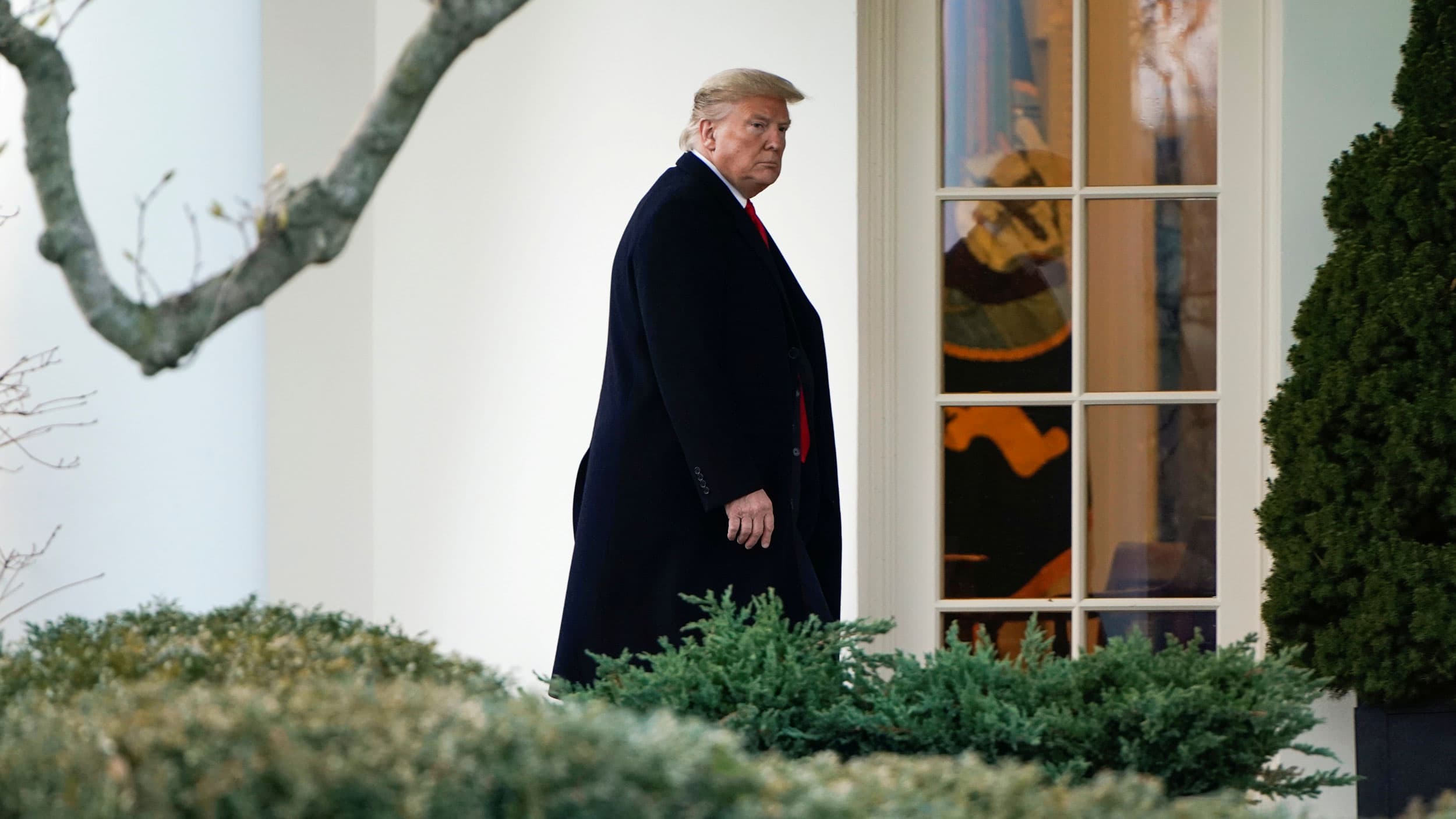 An older white man in a long black coat walks