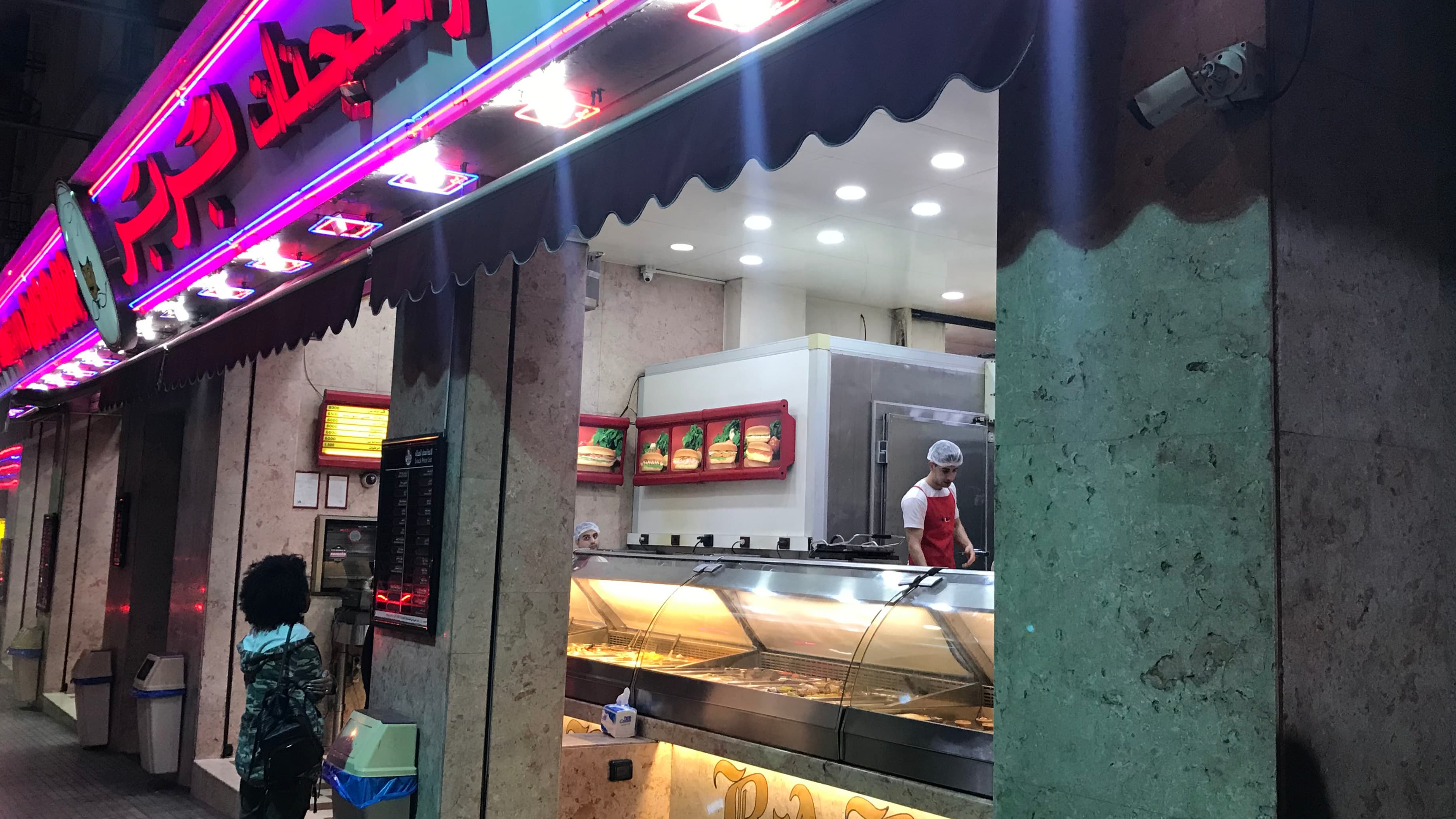 A woman stands in front of a brightly lit restaurant sign