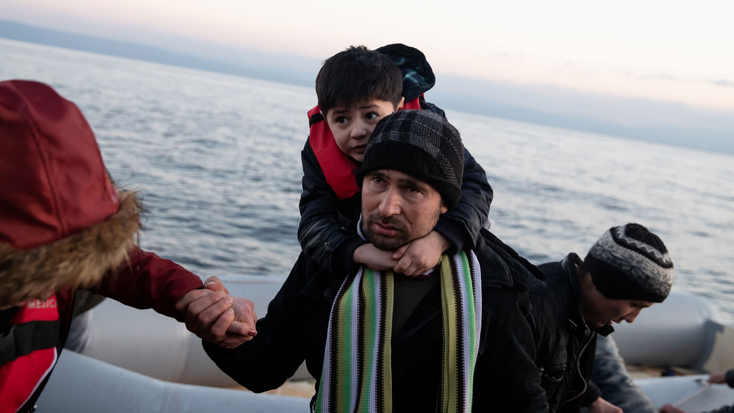 A man with a small boy on his back climb from a dinghy