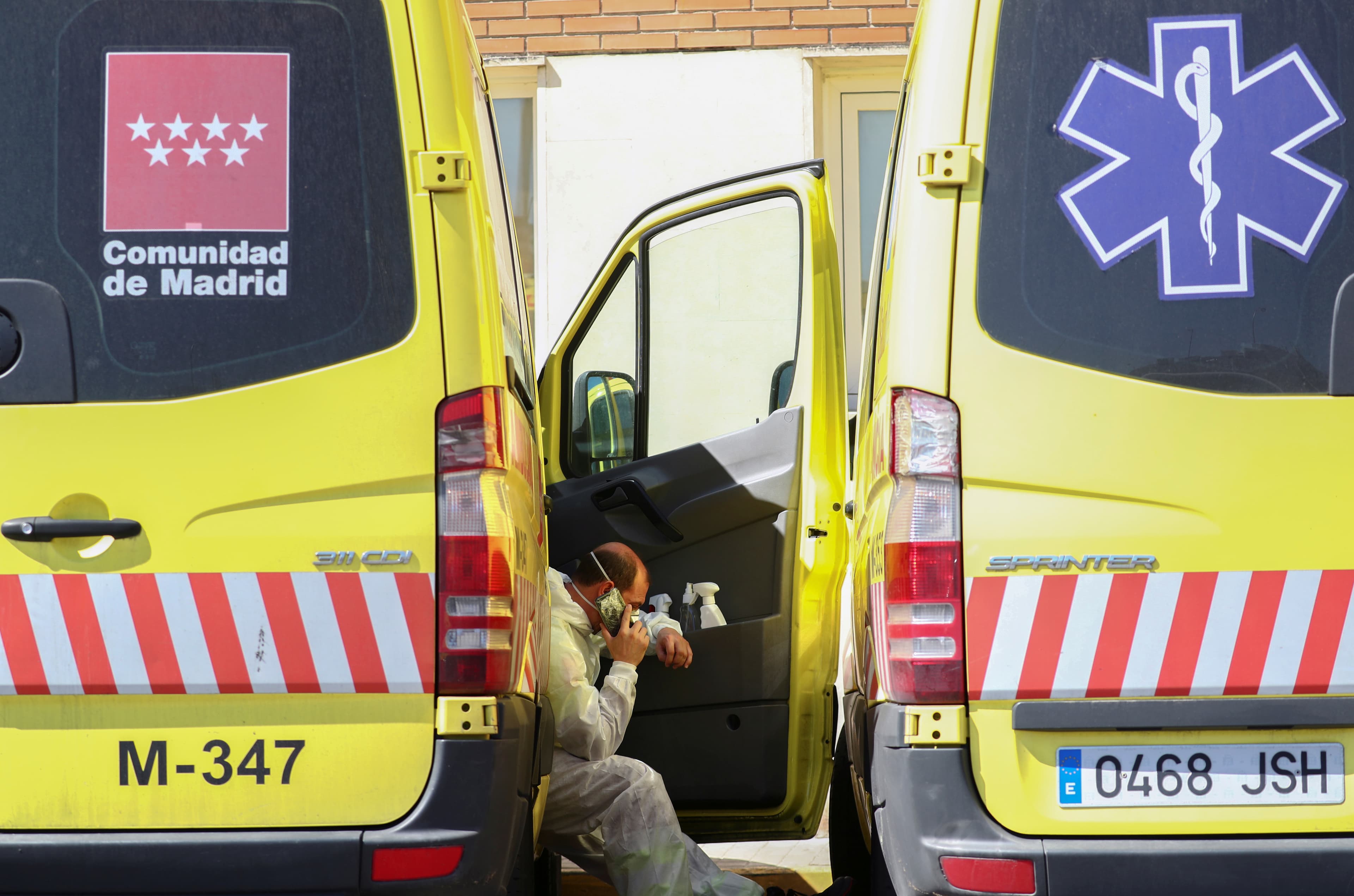 An ambulance driver rests between two vehicles and talks on the phone