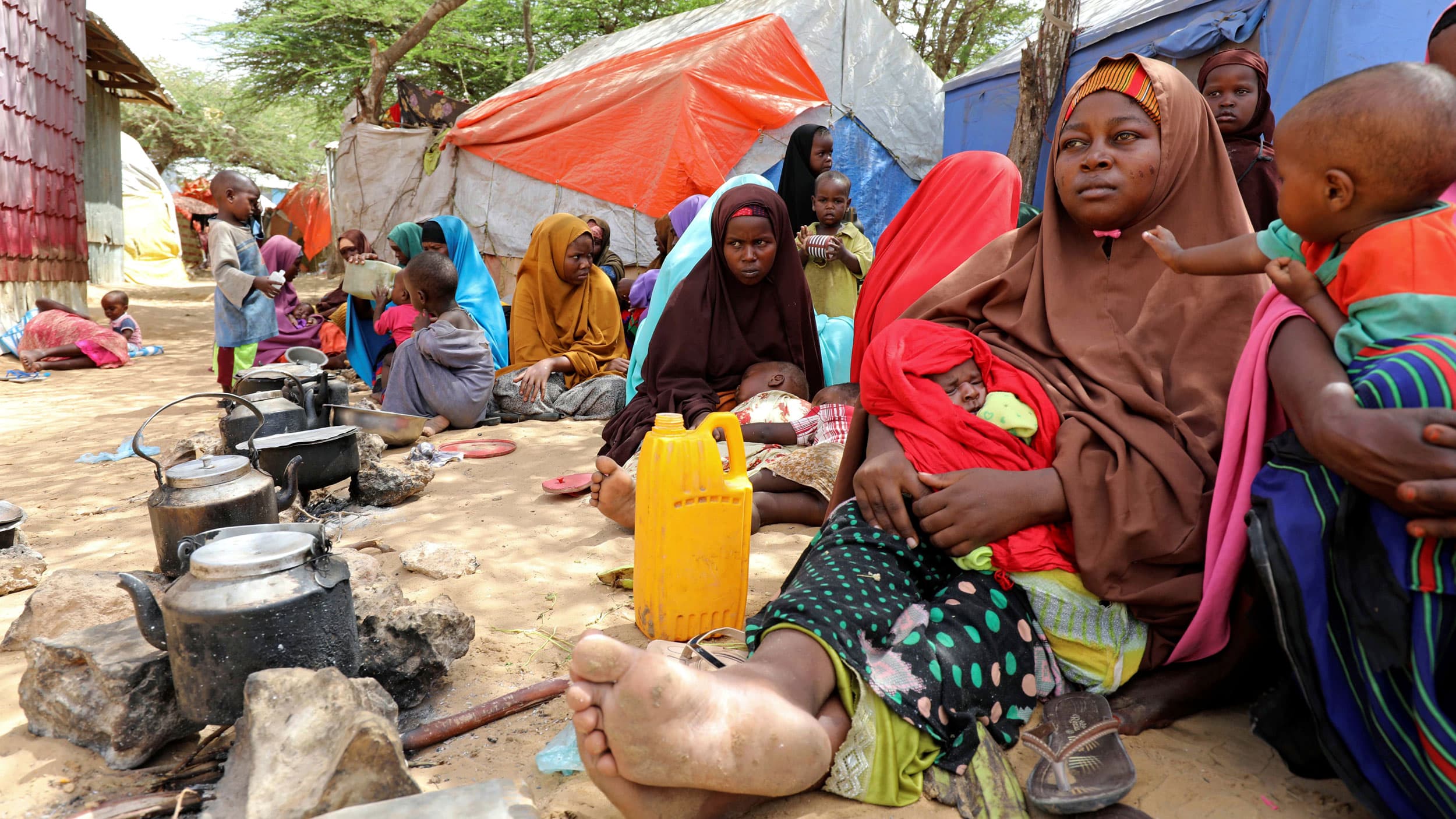 A woman and children in headscarves sit on the ground in front of tents