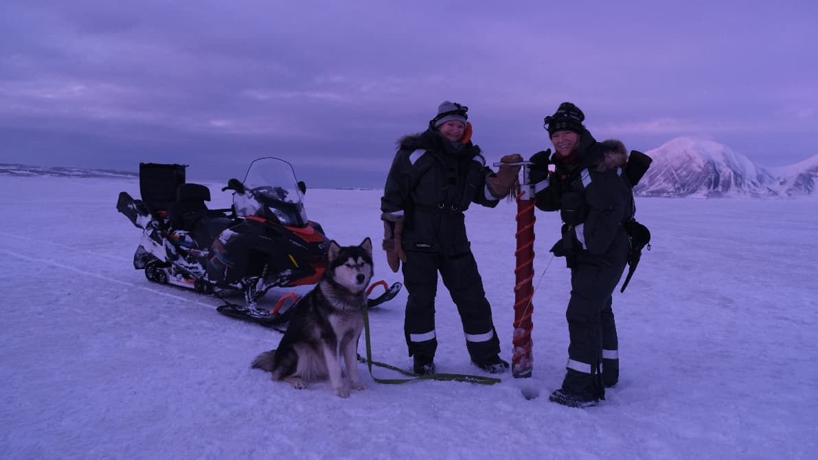 two women pose for a photo with a dog in the snow.