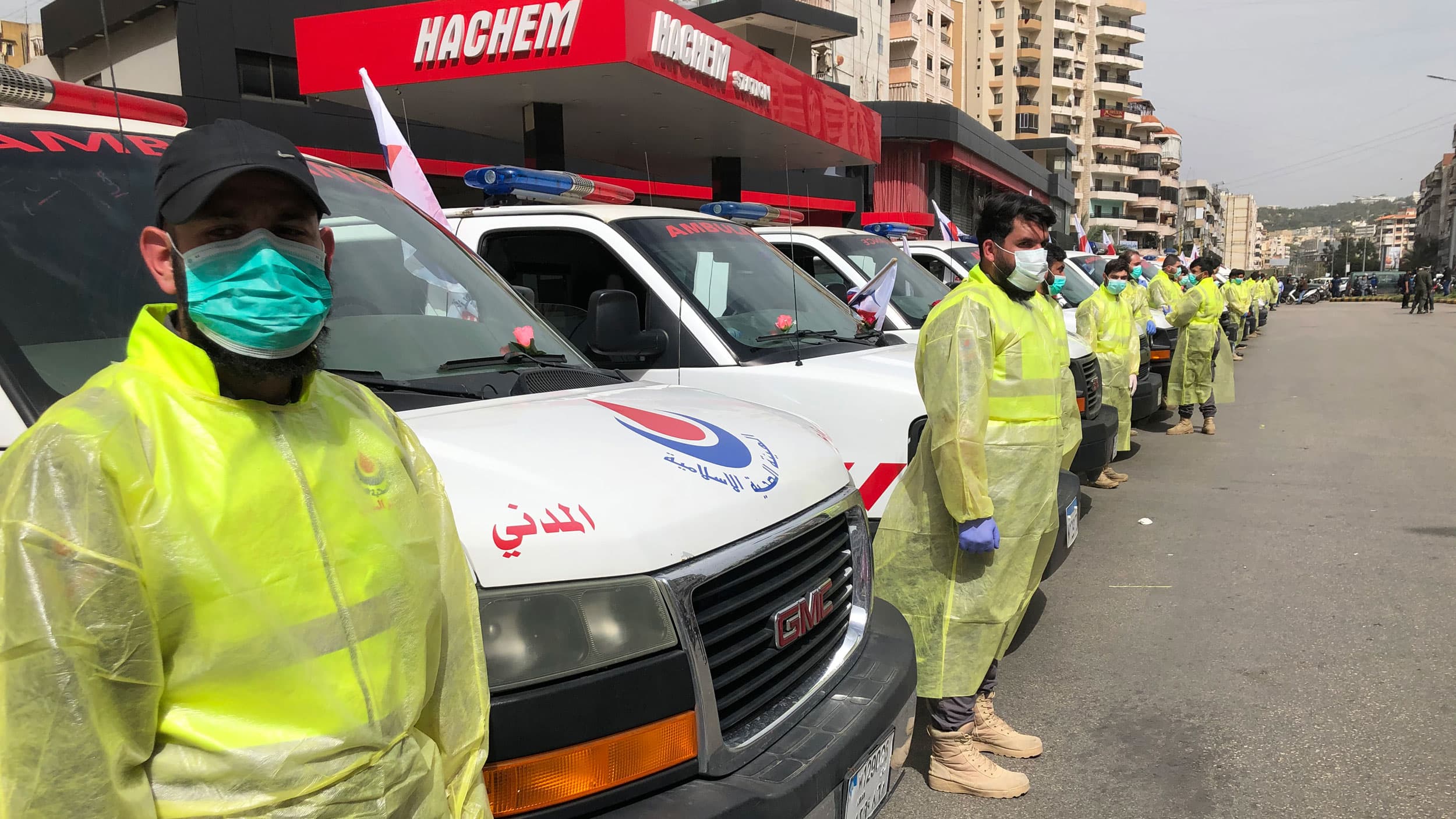 Men in personal protective gear stand in a line in front of vans.