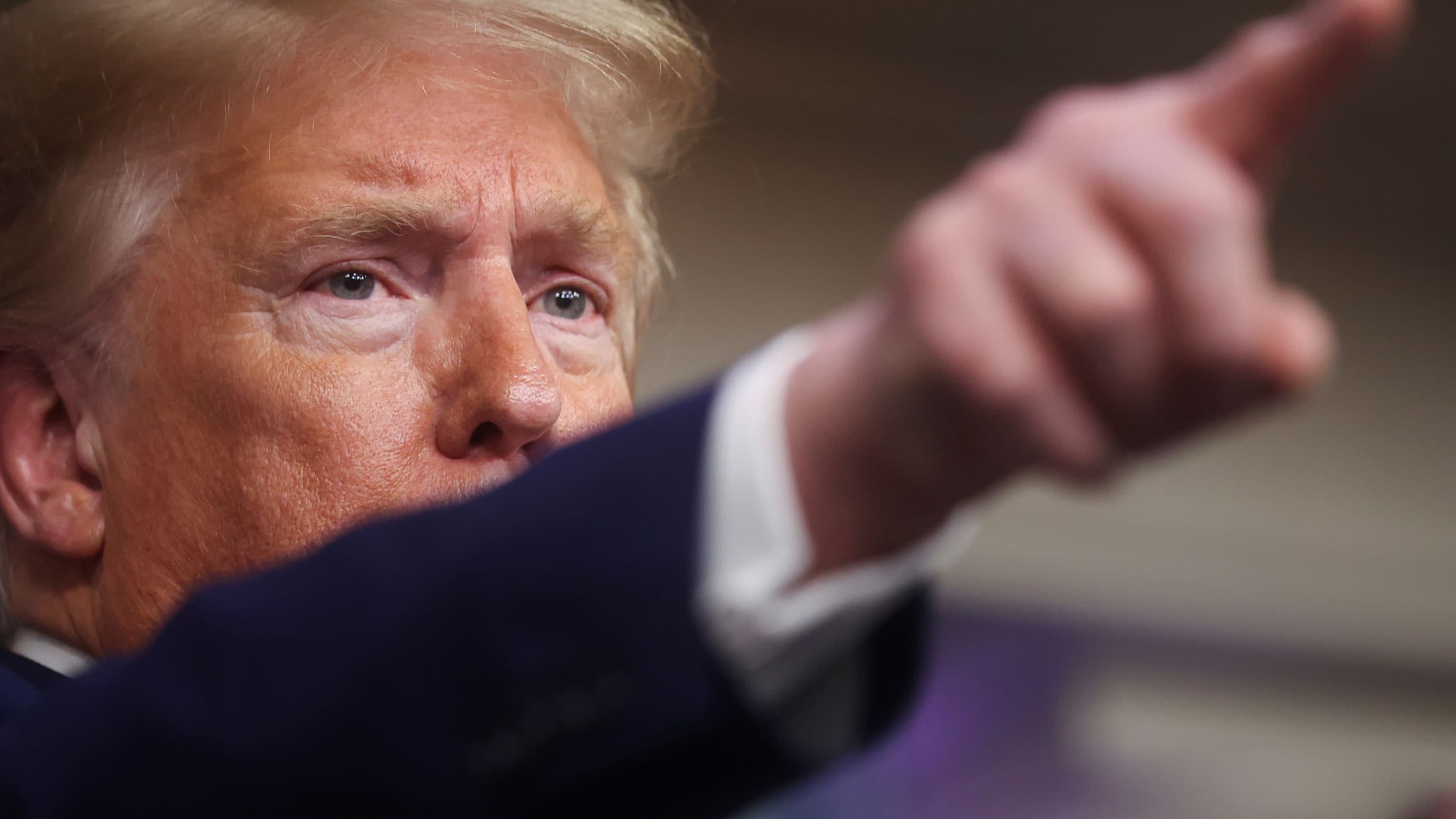 A close-up photograph of President Donald Trump shown from the side with his arm covering most of his face.